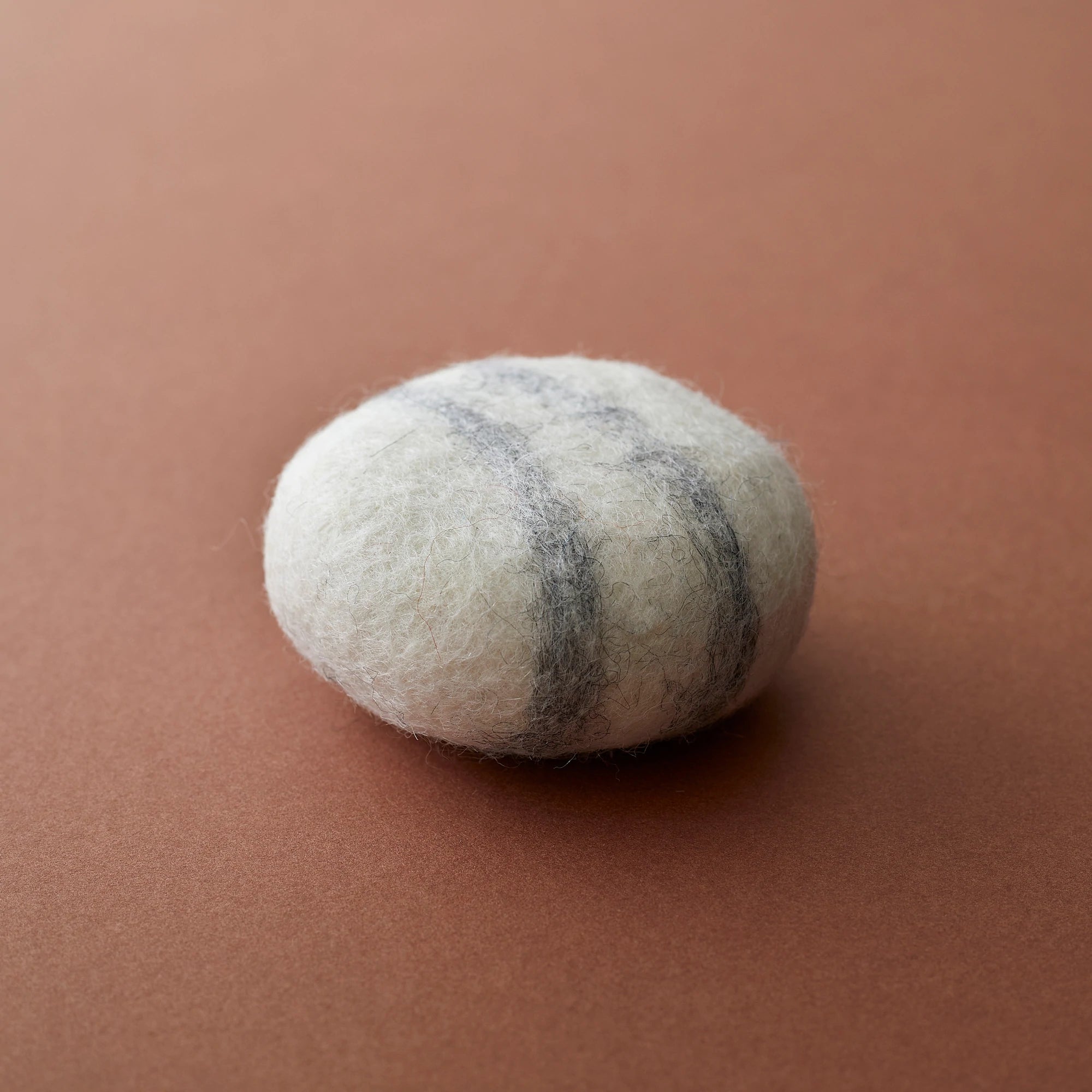 Round felted wool ball, off-white with dark gray stripes.