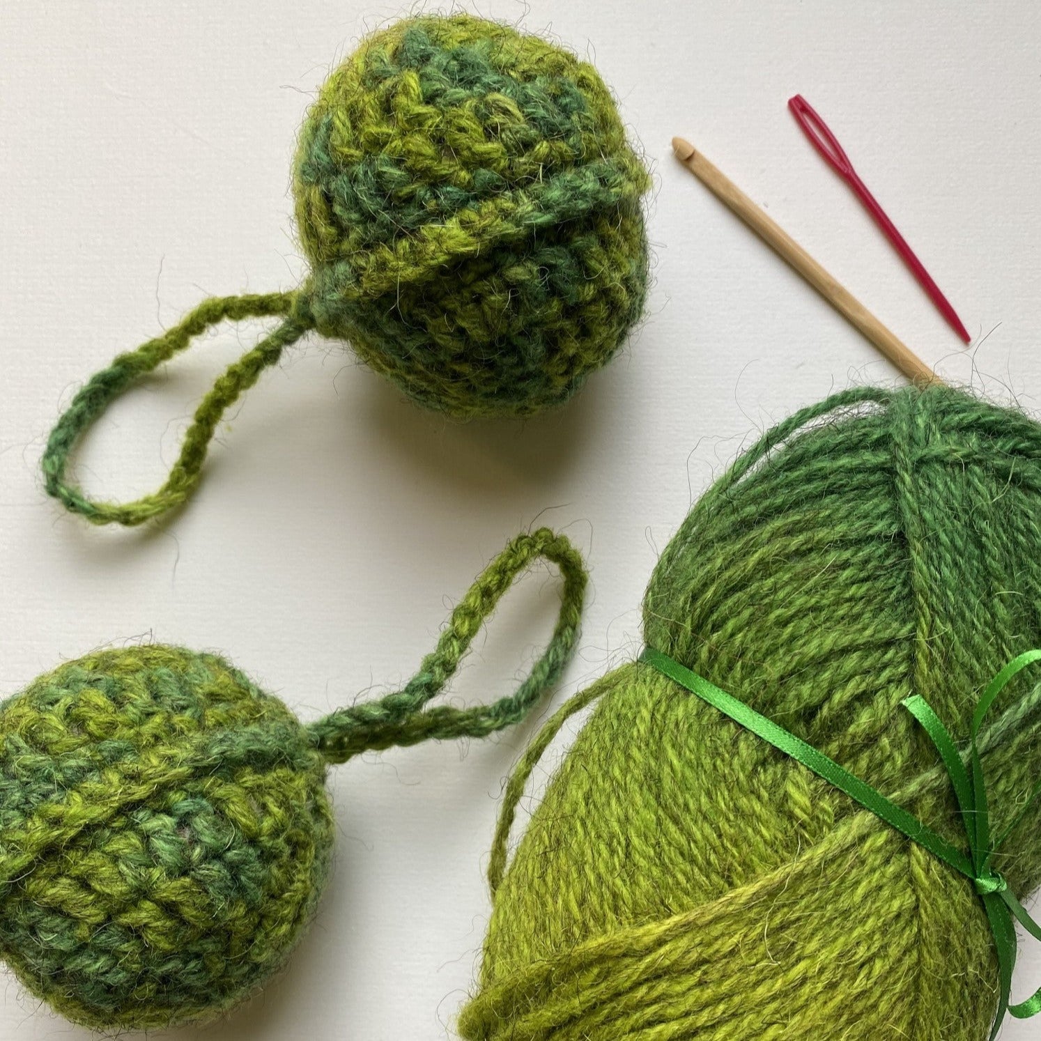 Two small, crocheted green ornaments with loops for hanging, and a ball of green yarn.