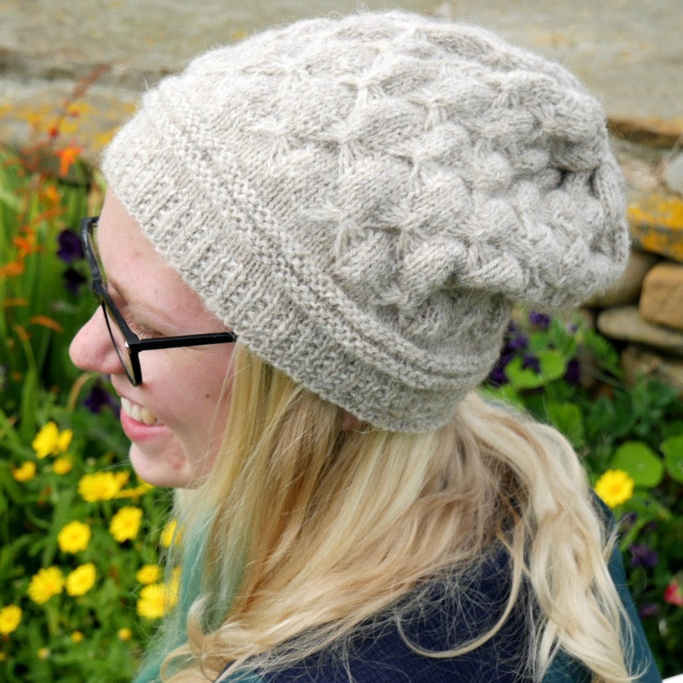 Light beige hand-knitted beanie with a textured cable pattern.