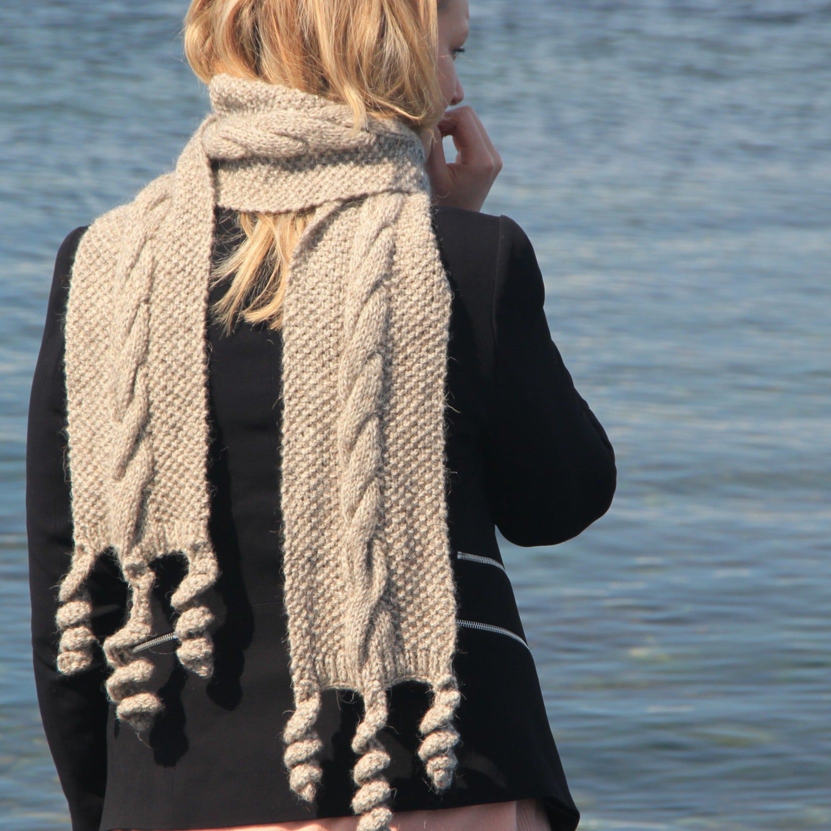 Beige hand-knitted cable-knit scarf with textured tassels.