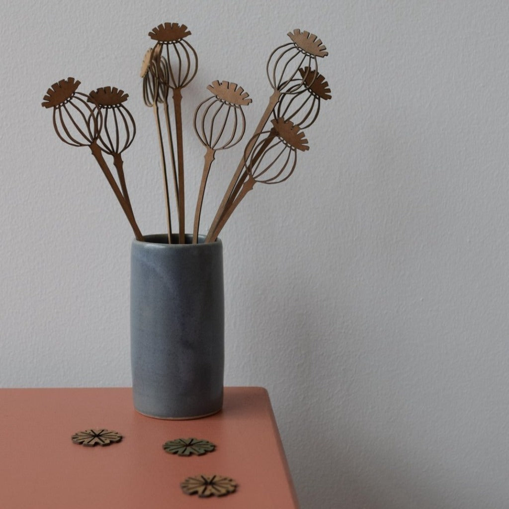 Wooden poppy seed head decorations in a gray ceramic vase.