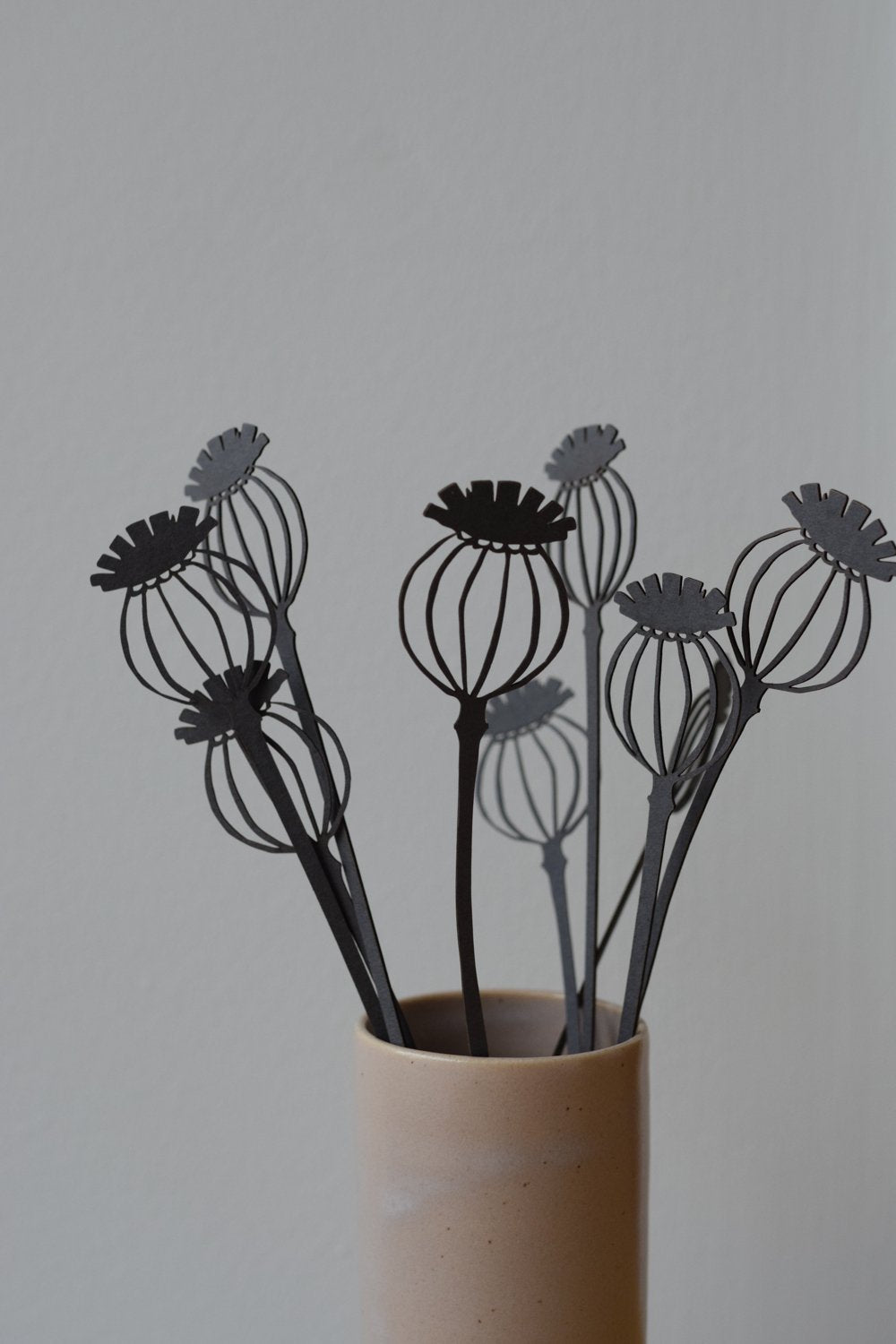Dark gray paper cut-out poppy seed heads in a light beige vase.