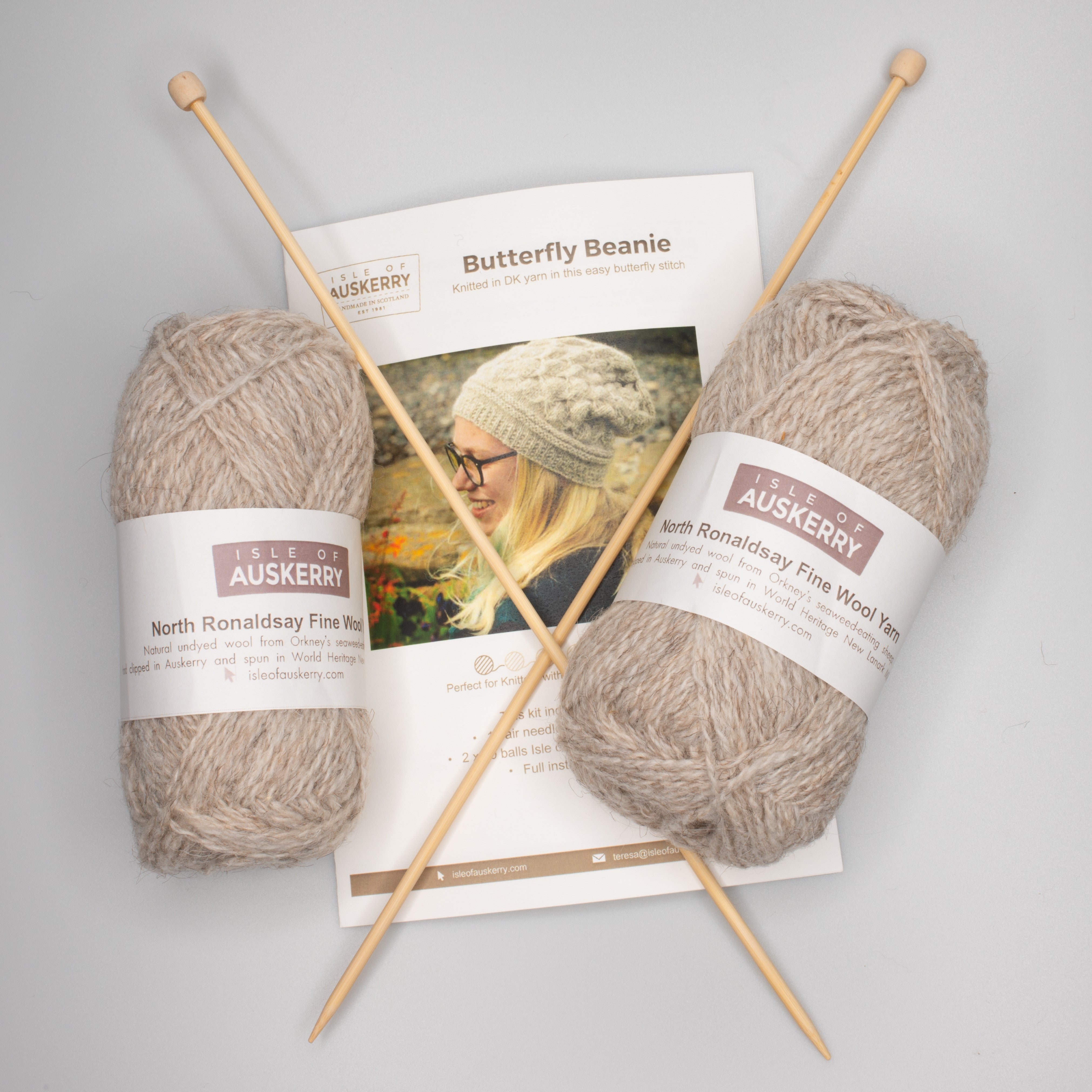 Two balls of light beige North Ronaldsay Fine Wool yarn, wooden knitting needles, and a pattern for a butterfly beanie.