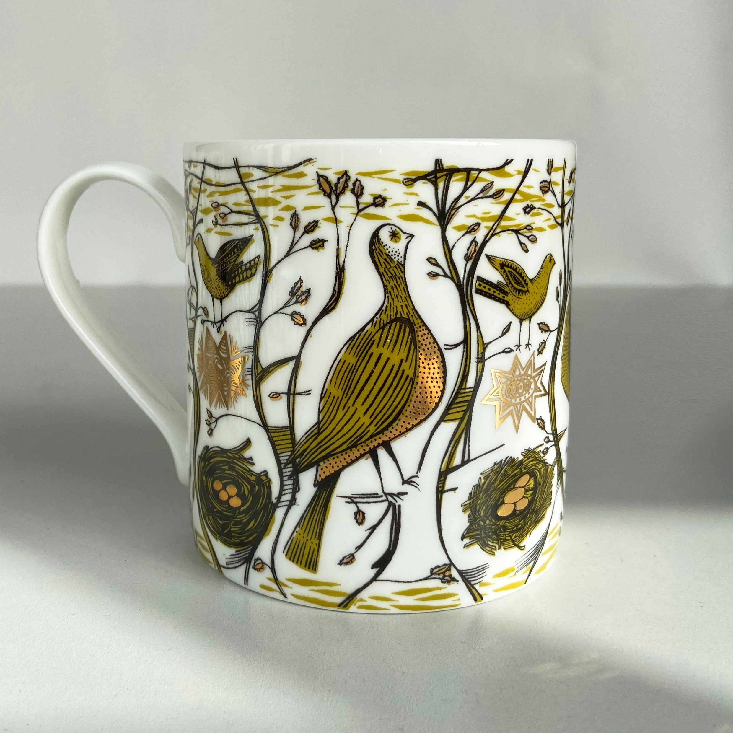 White mug with gold and olive green bird illustration.