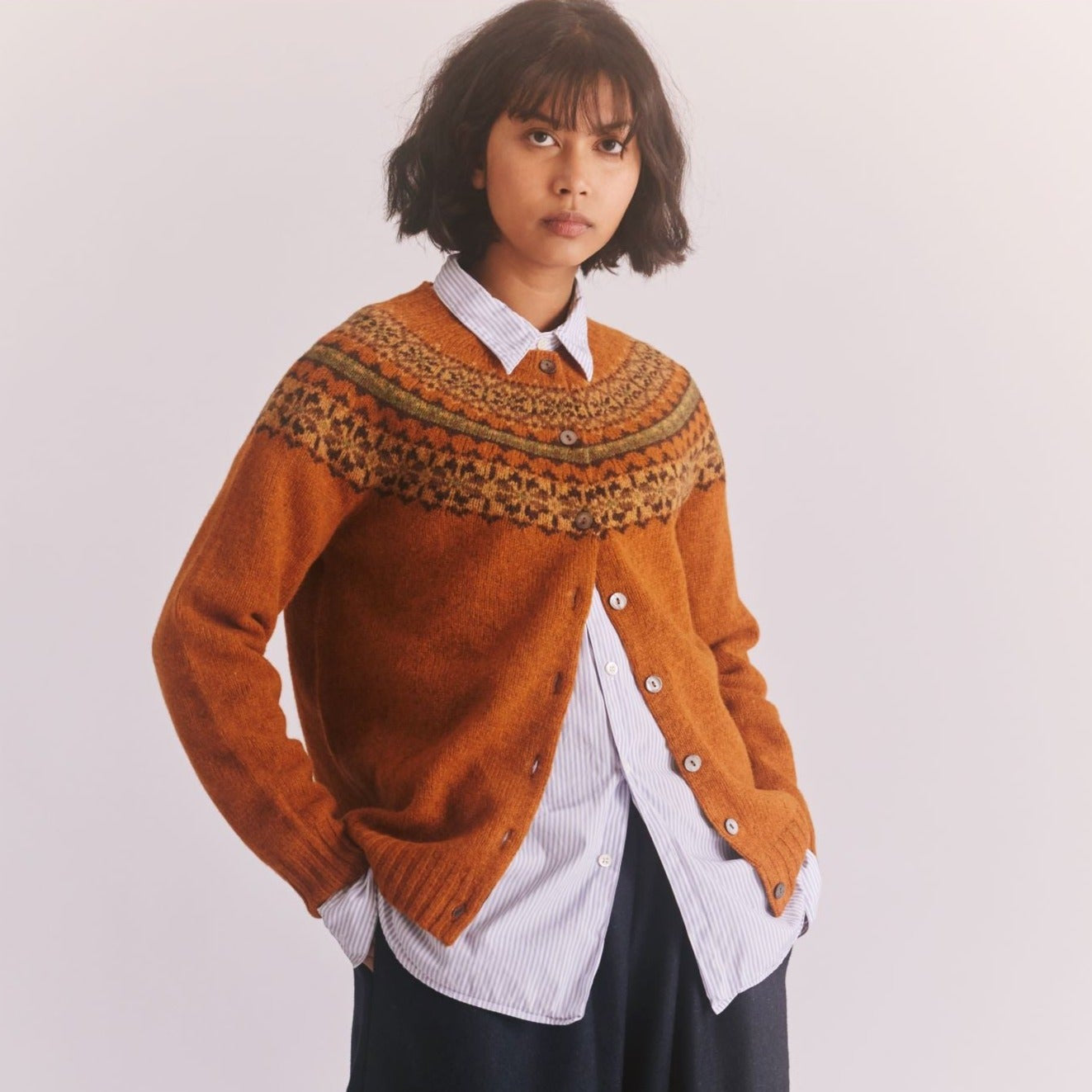 a female model standing with hands in pockets wetaing a Harley of Scotland Ladies Cardigan - Vintage Orange