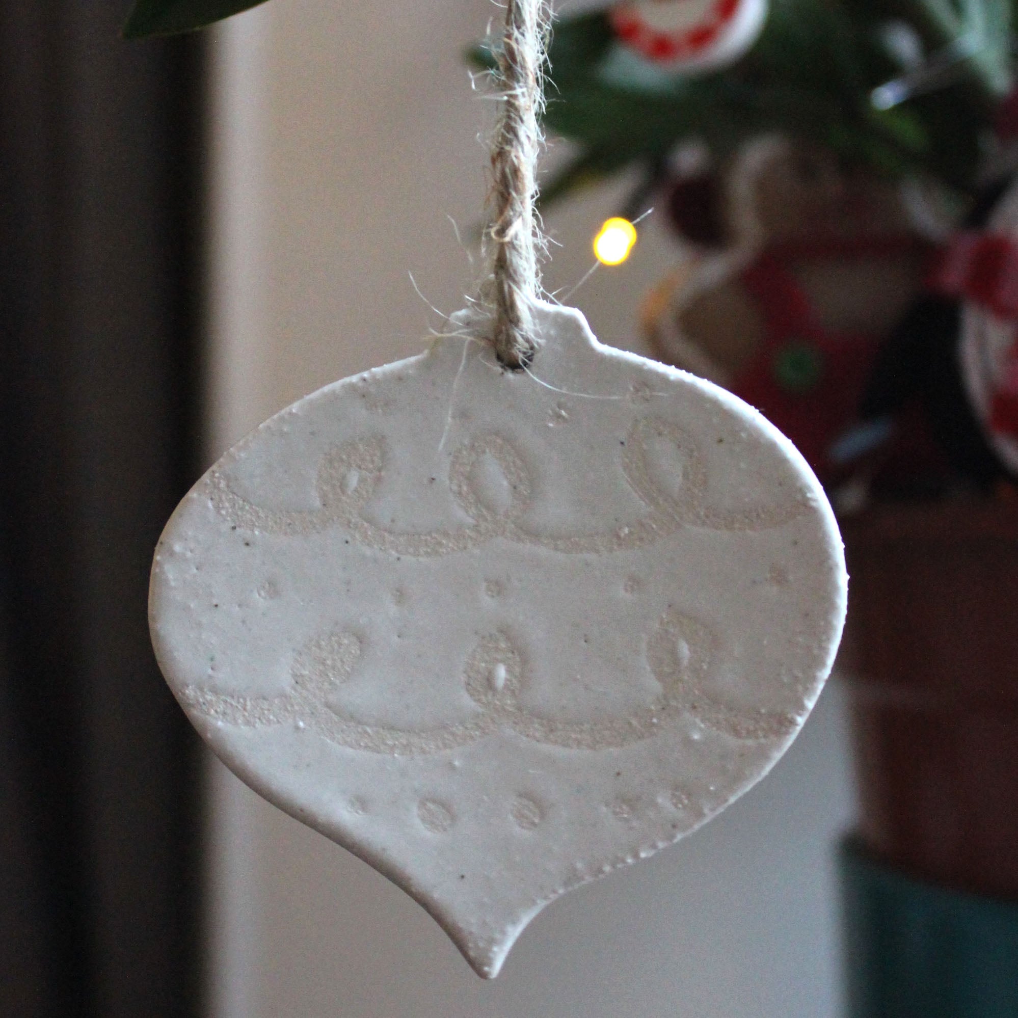 White ceramic Christmas ornament shaped like a teardrop, featuring an embossed, repeating pattern.