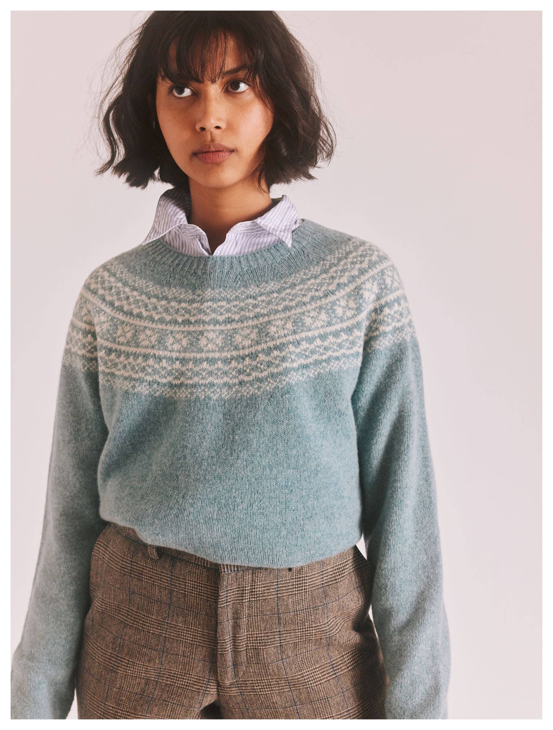 Teal blue crewneck sweater with a fair isle-style pattern across the upper chest. Soft, textured knit.
