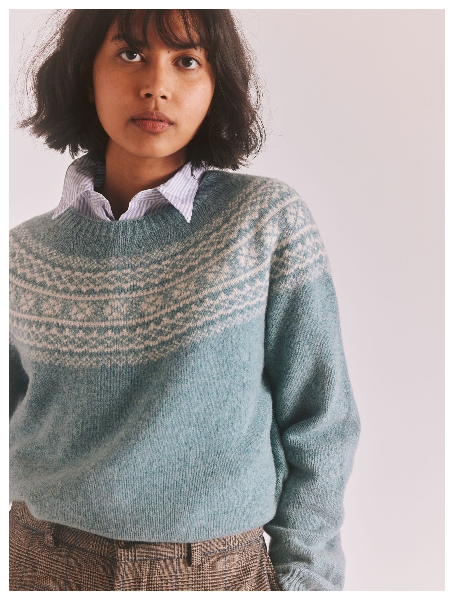 Teal blue crewneck sweater with a fair isle-style pattern across the shoulders. Soft, fluffy knit texture.