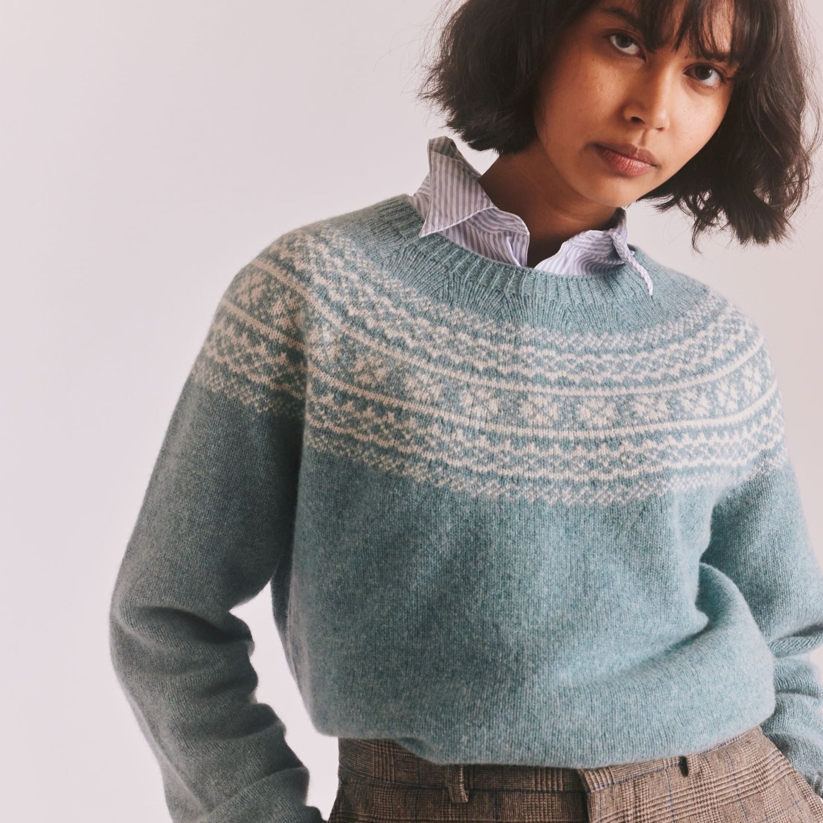 Teal crewneck sweater with a fair isle-style pattern across the shoulders. Soft, knit texture.