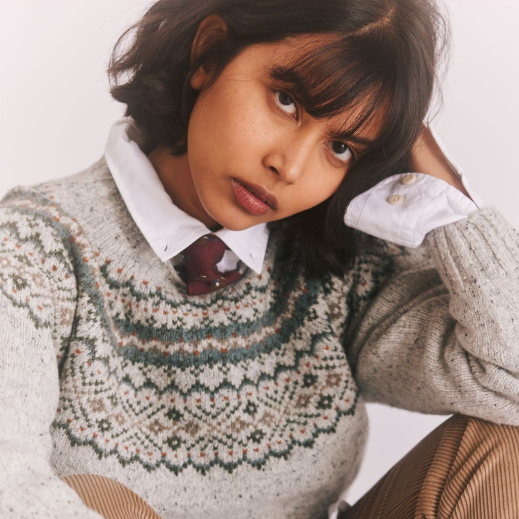 a female model, seated with elbows resting on knees, and head in hand, wearing a Harley of Scotland Fairisle Jumper - Islay