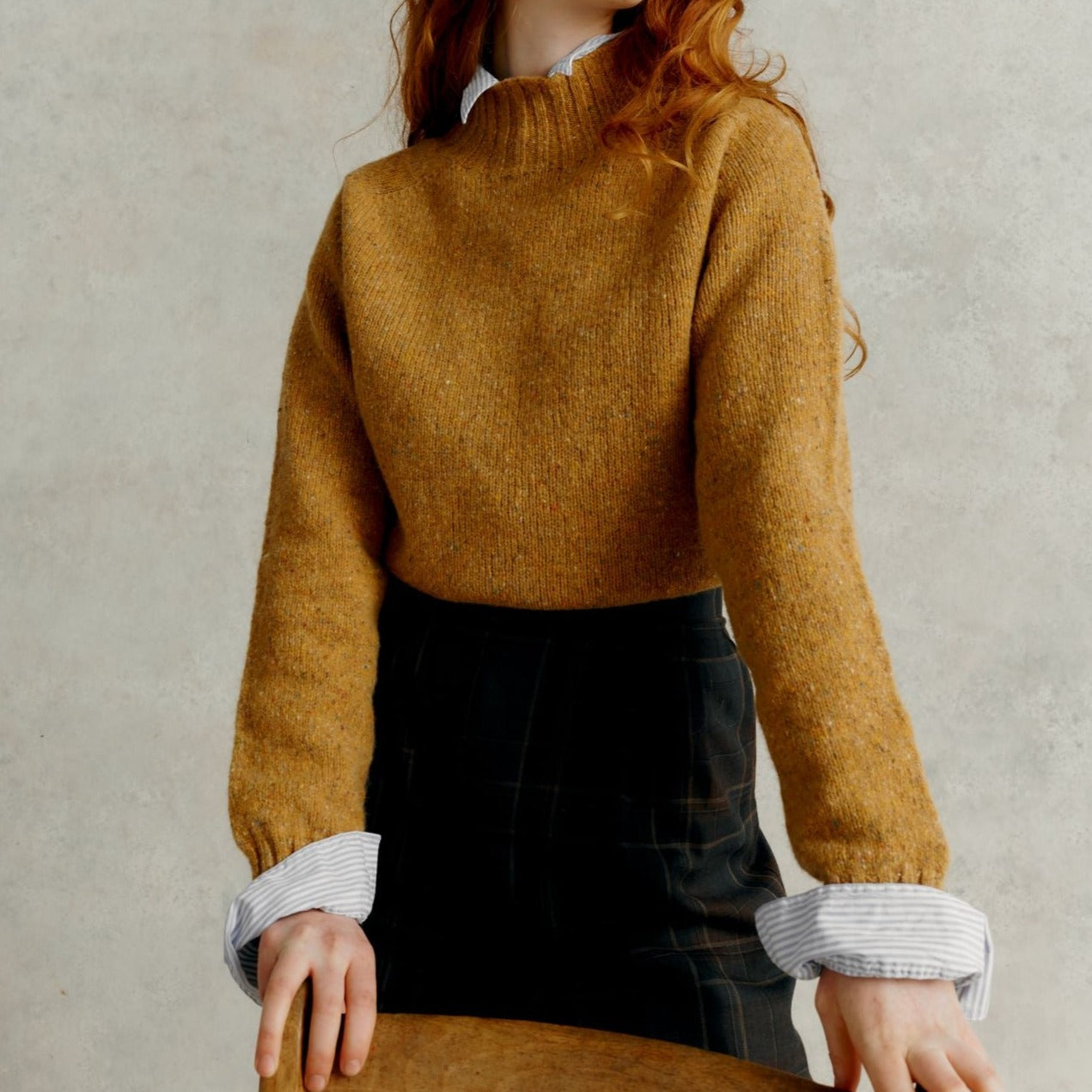 a red haired female model resting forward against a chair, wearing a Harley of Scotland Turtleneck Sweater - Barra