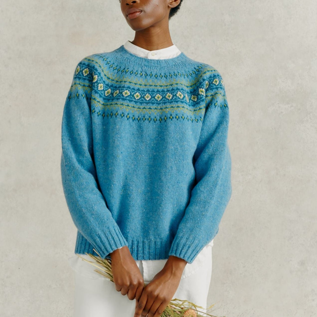 a female model holding a bunch of dried flowers, wearing white linen trousers and a Harley of Scotland Fairisle Jumper - Coll
