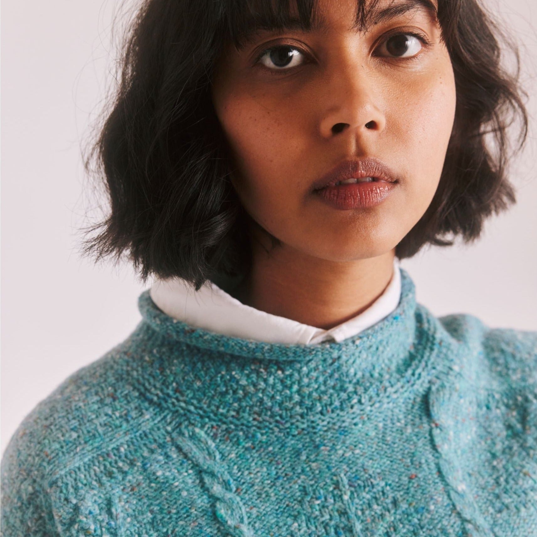 Teal cable-knit sweater with speckled texture, shown on a model.