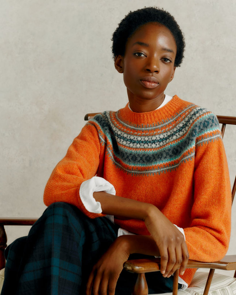 a female model seated in a wooden chair with legs and arms crossed, wearing a Harley of Scotland Yoke Soft Jumper - Jaffa