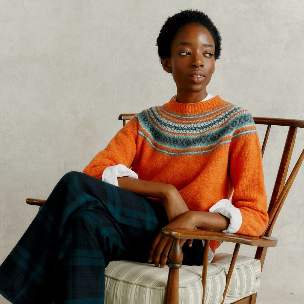 a female model seated in a wooden chair with legs crossed, wearing a Harley of Scotland Yoke Soft Jumper - Jaffa