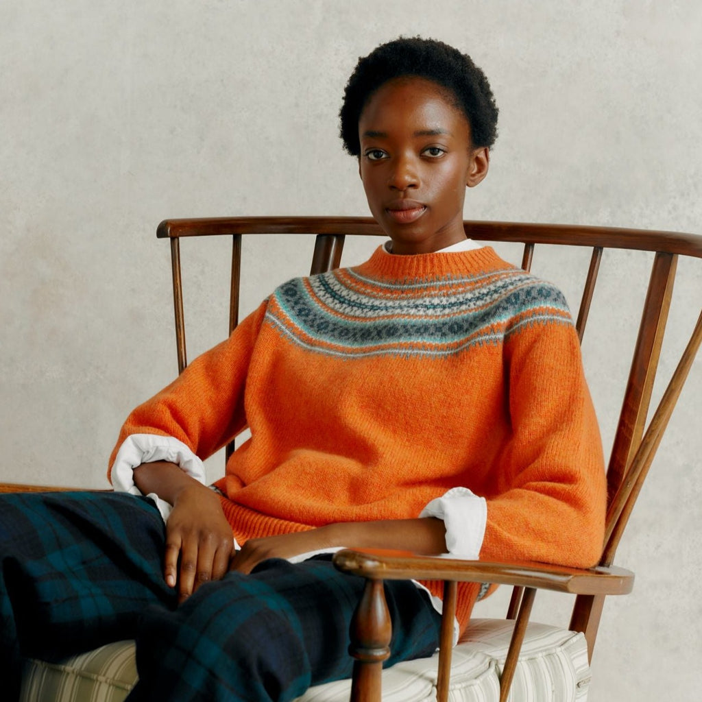 a female model seated in a wooden chair, wearing a Harley of Scotland Yoke Soft Jumper - Jaffa