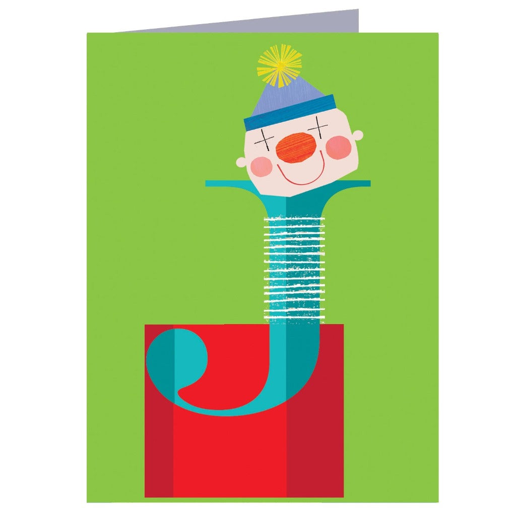 Greeting card featuring a stylized clown's face atop a teal letter J, set against a red and green background.