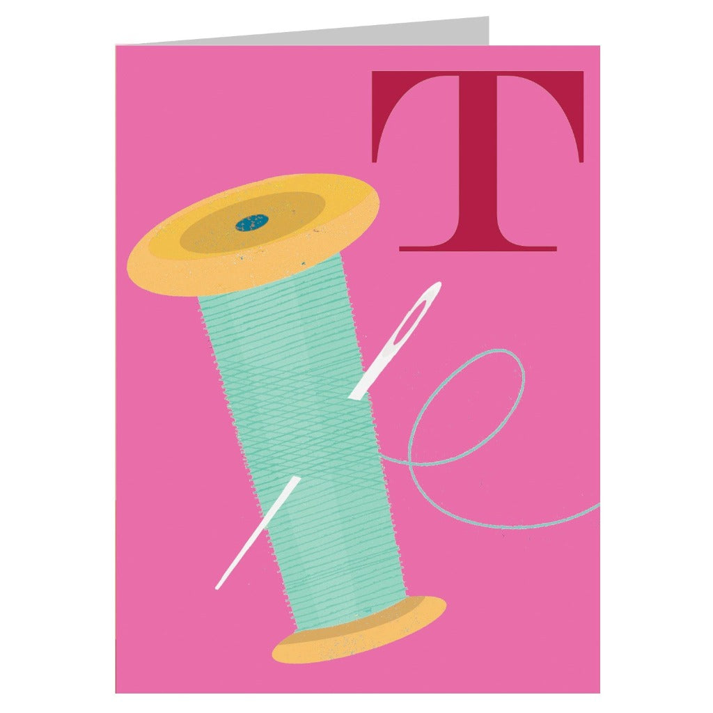 A teal spool of thread with a needle and thread, and a large maroon "T," on a pink background.