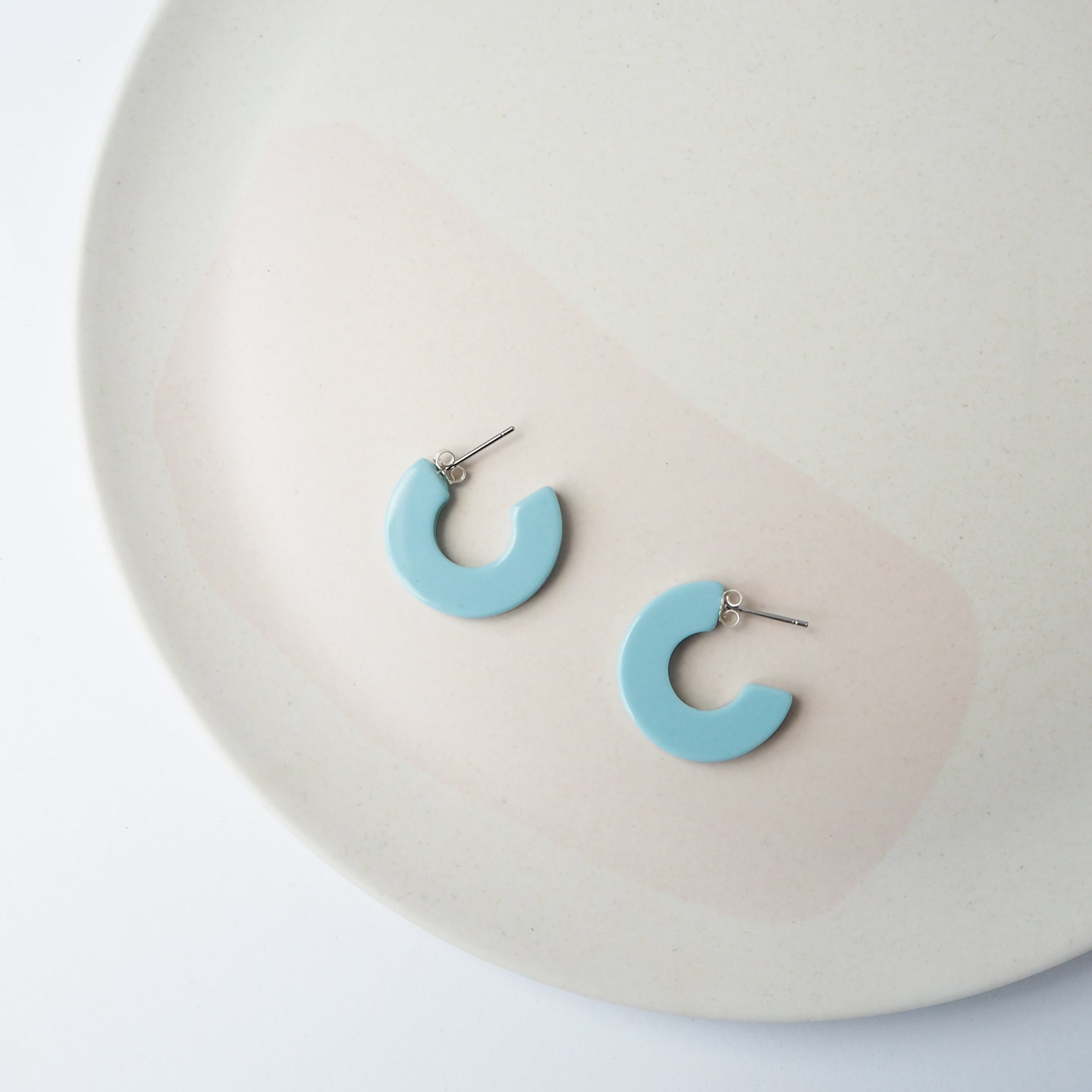 Pair of light blue semi-circular hoop earrings with silver posts.