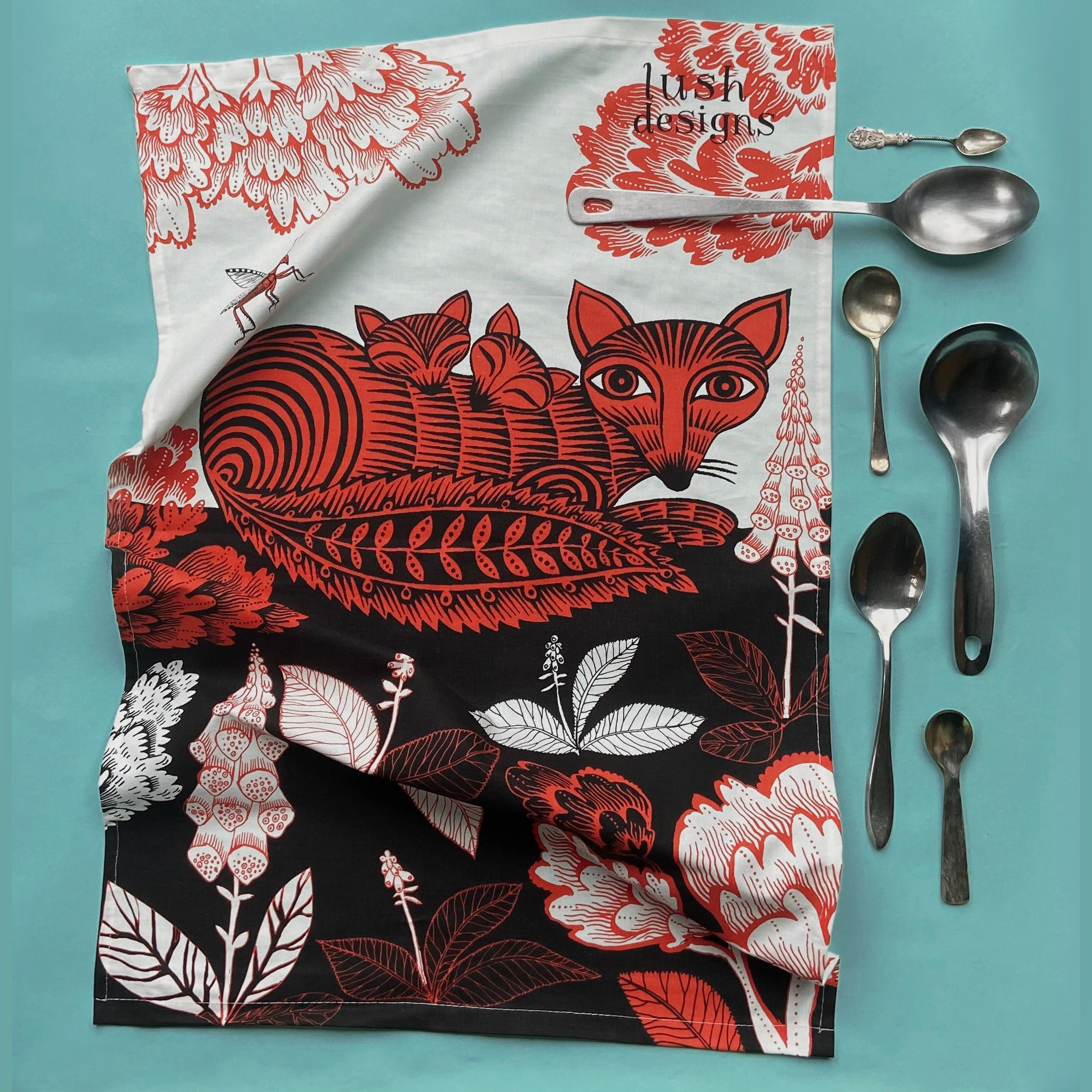Tea towel featuring a stylized fox with kits amidst red and black floral designs.