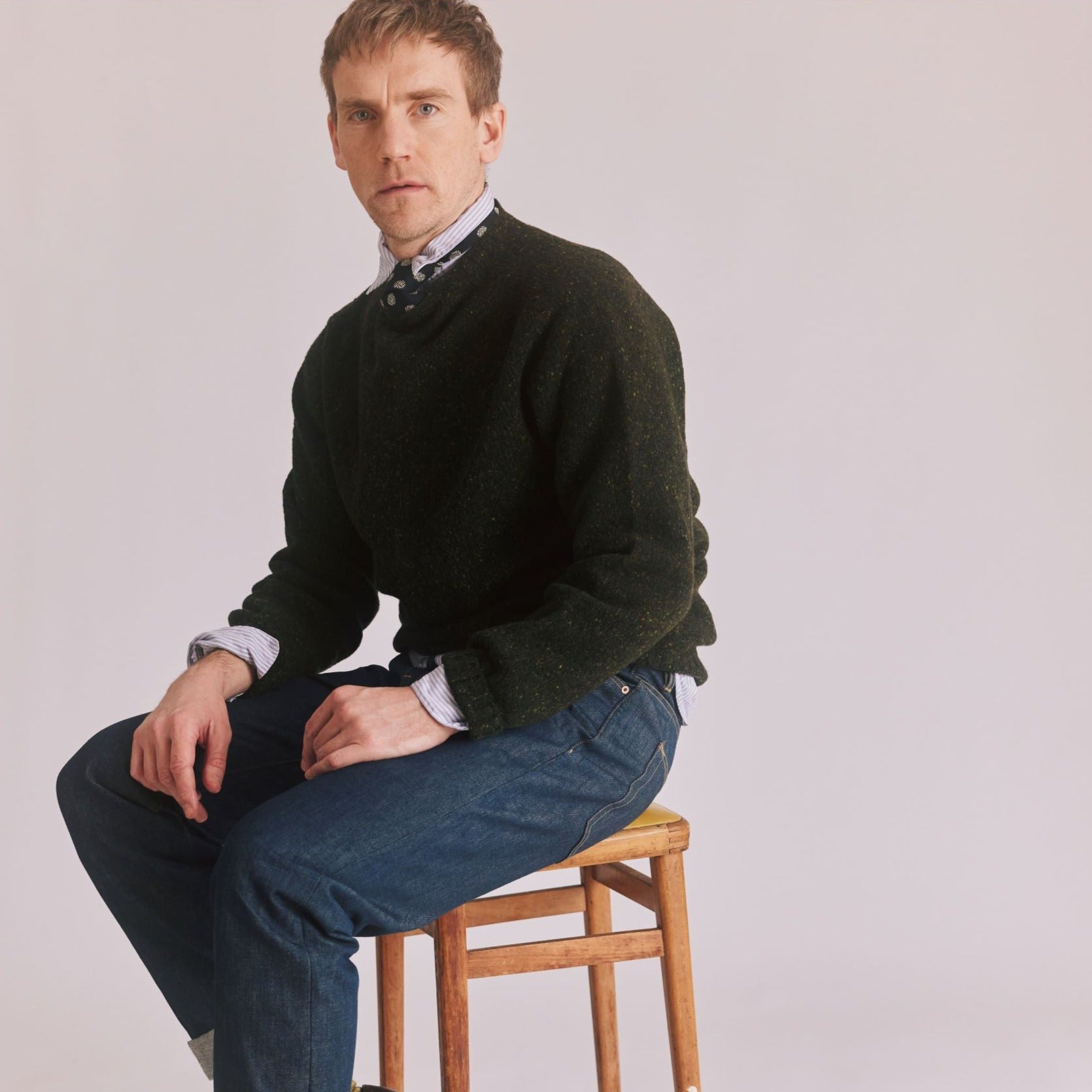 man sat on stool wearing a Harley of Scotland Men's Flecked Jumper in Harris colourway