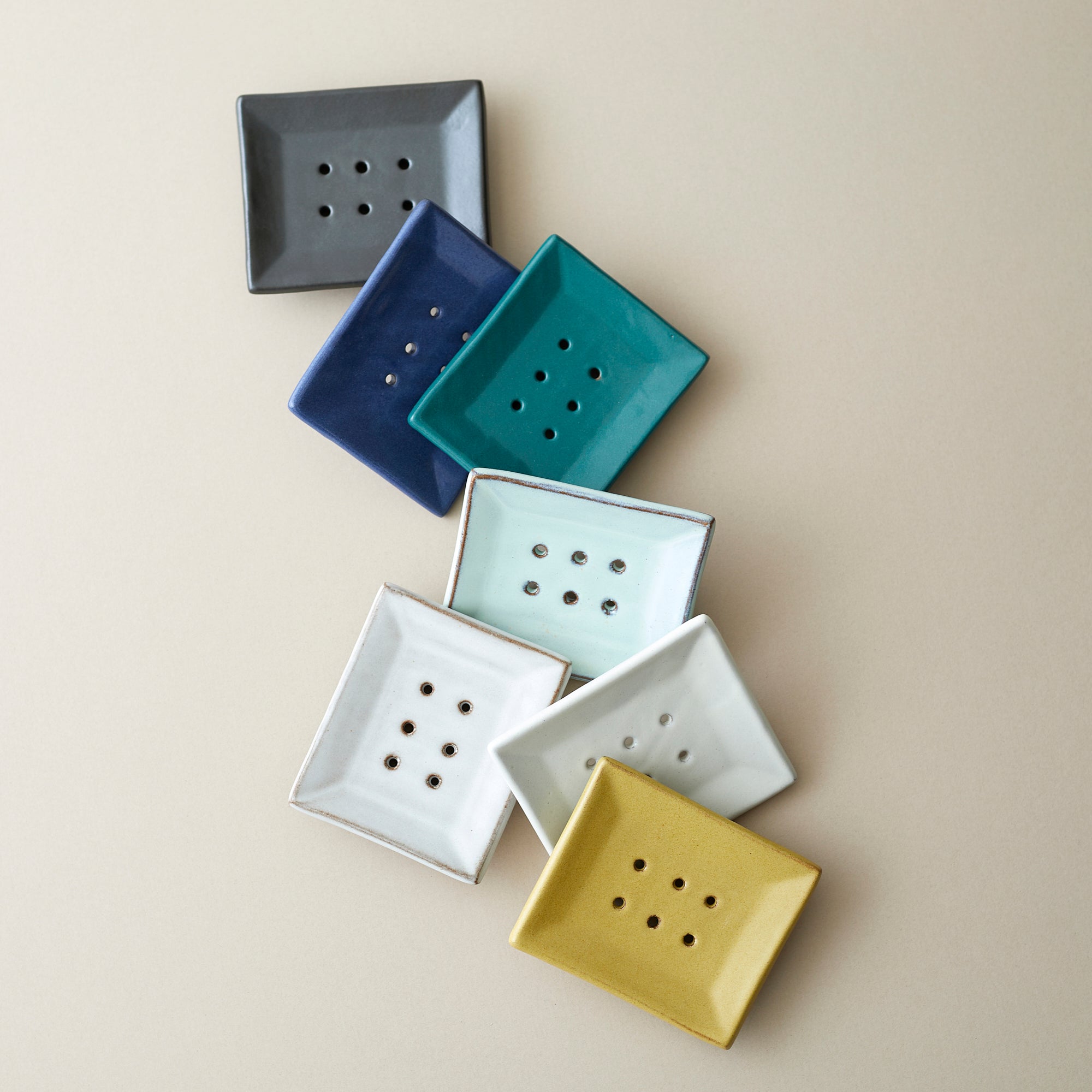 Collection of square ceramic soap dishes in various pastel colors. Each dish features drainage holes.