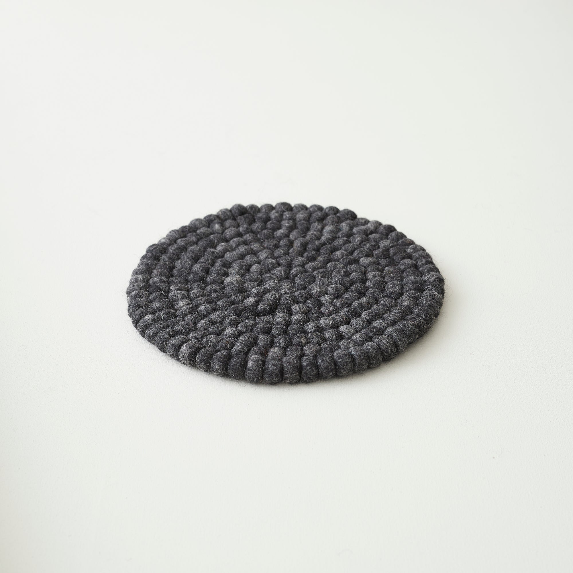 Dark gray round felt coaster, textured with small, densely packed balls of wool.