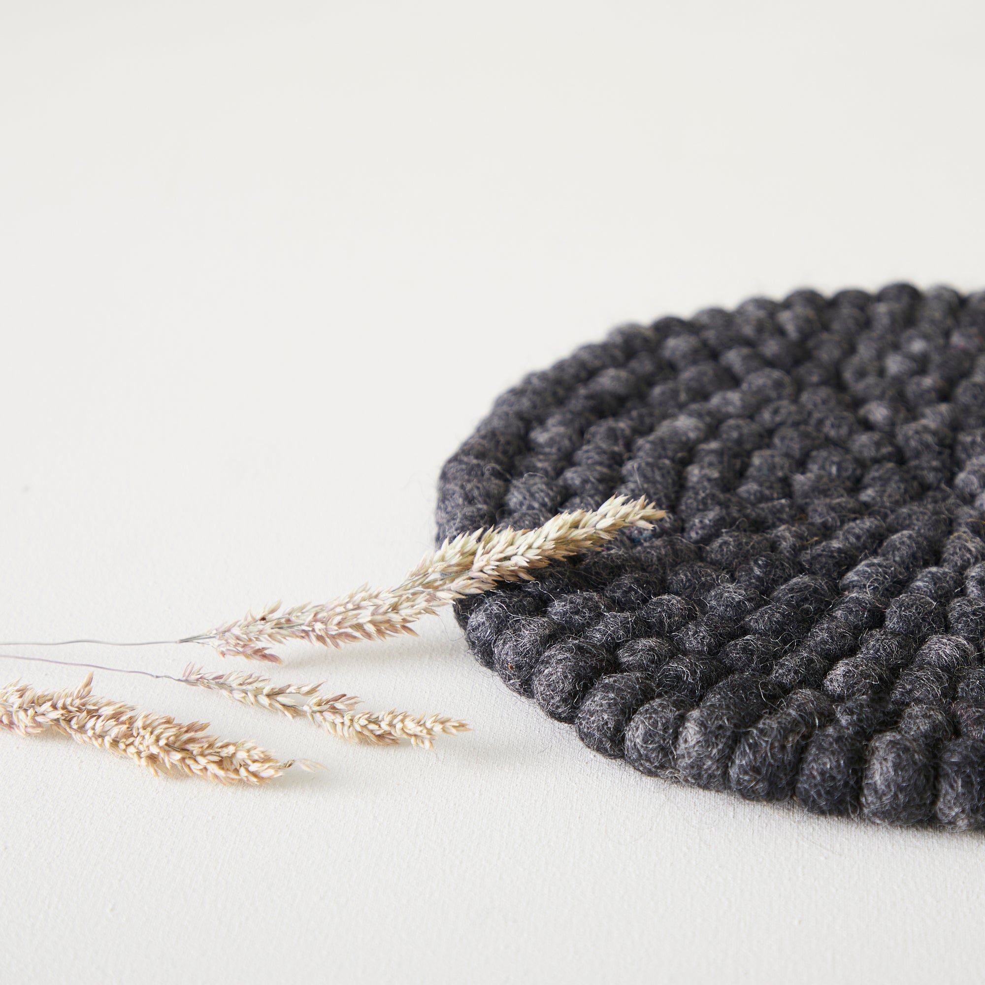Dark gray round wool felt coaster with a textured, looped surface.