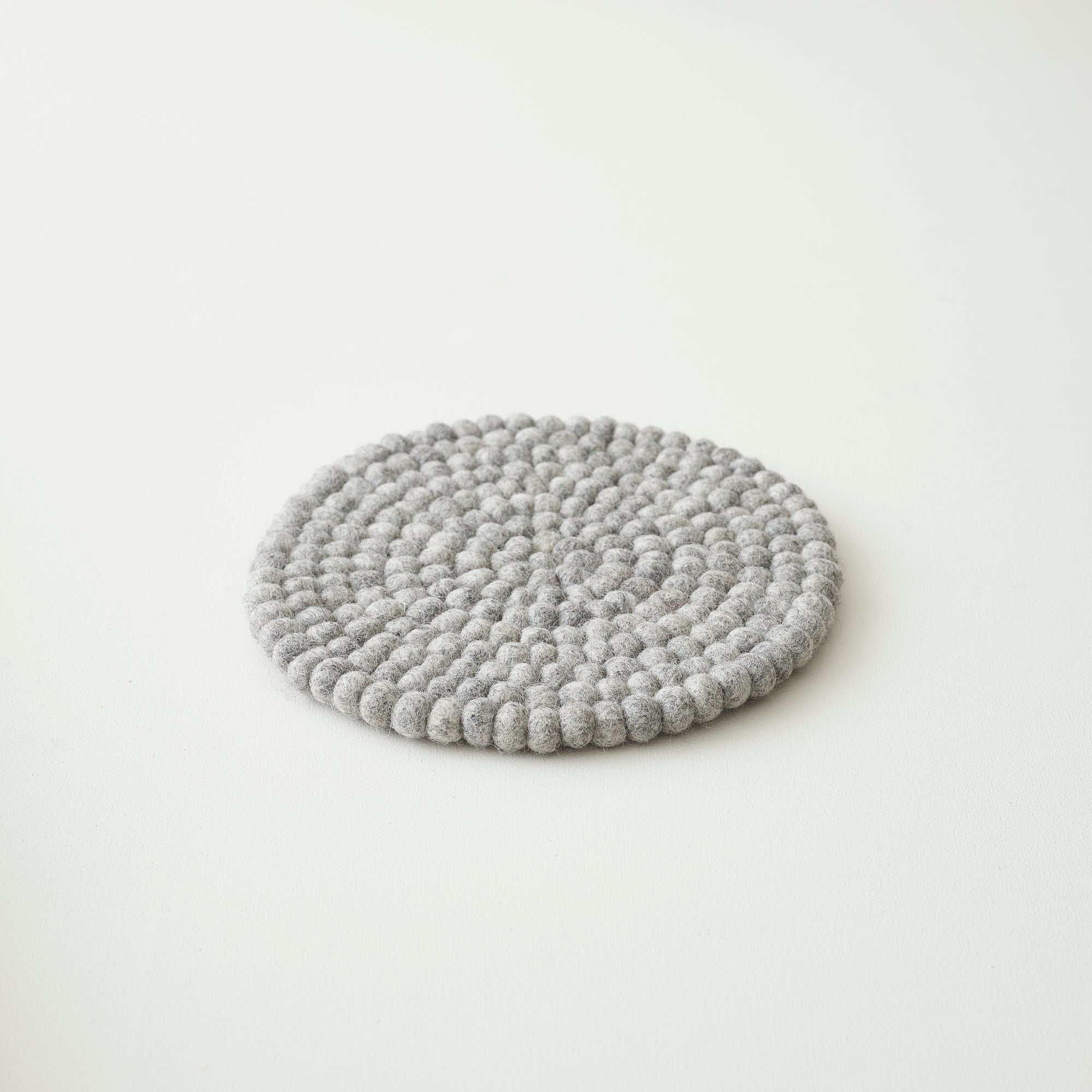 Round gray felt coaster made of small, densely packed balls of wool.