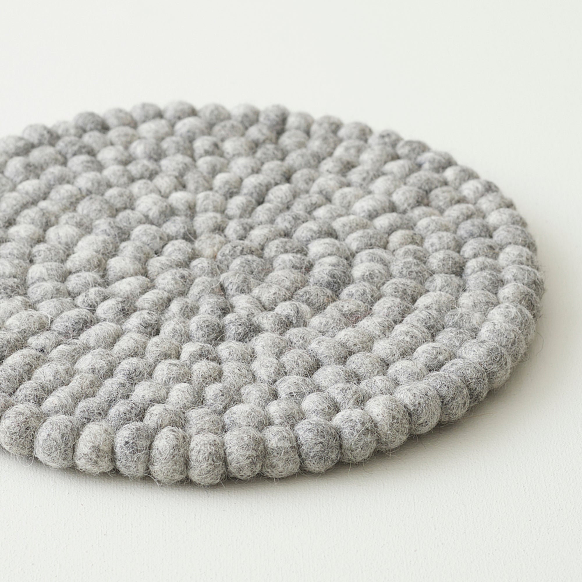 Round gray felt coaster made of densely packed small balls of wool.
