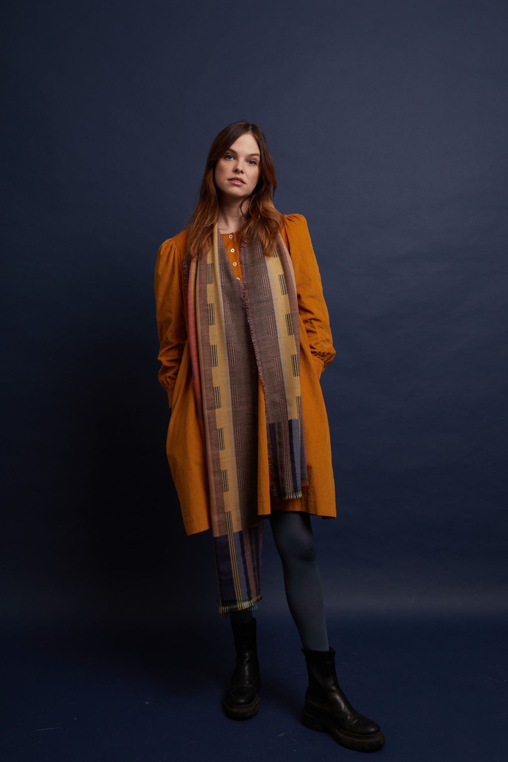 A long, multicolored woven scarf with a textured pattern, draped over a mustard-yellow dress.