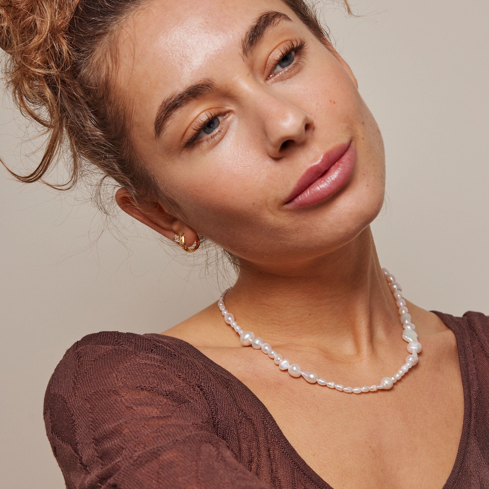 Delicate pearl necklace featuring small and larger baroque pearls on a brown knit top.