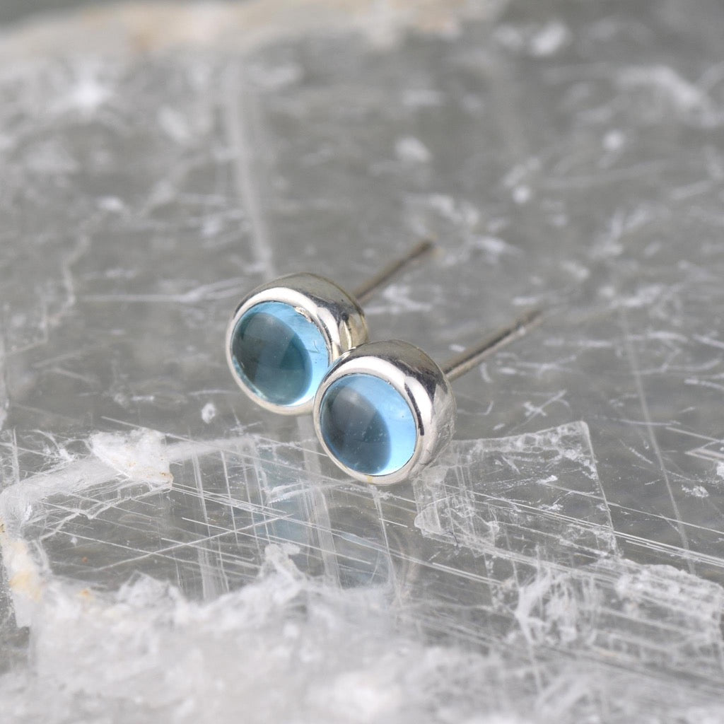 Pair of silver stud earrings with round, light blue gemstones.
