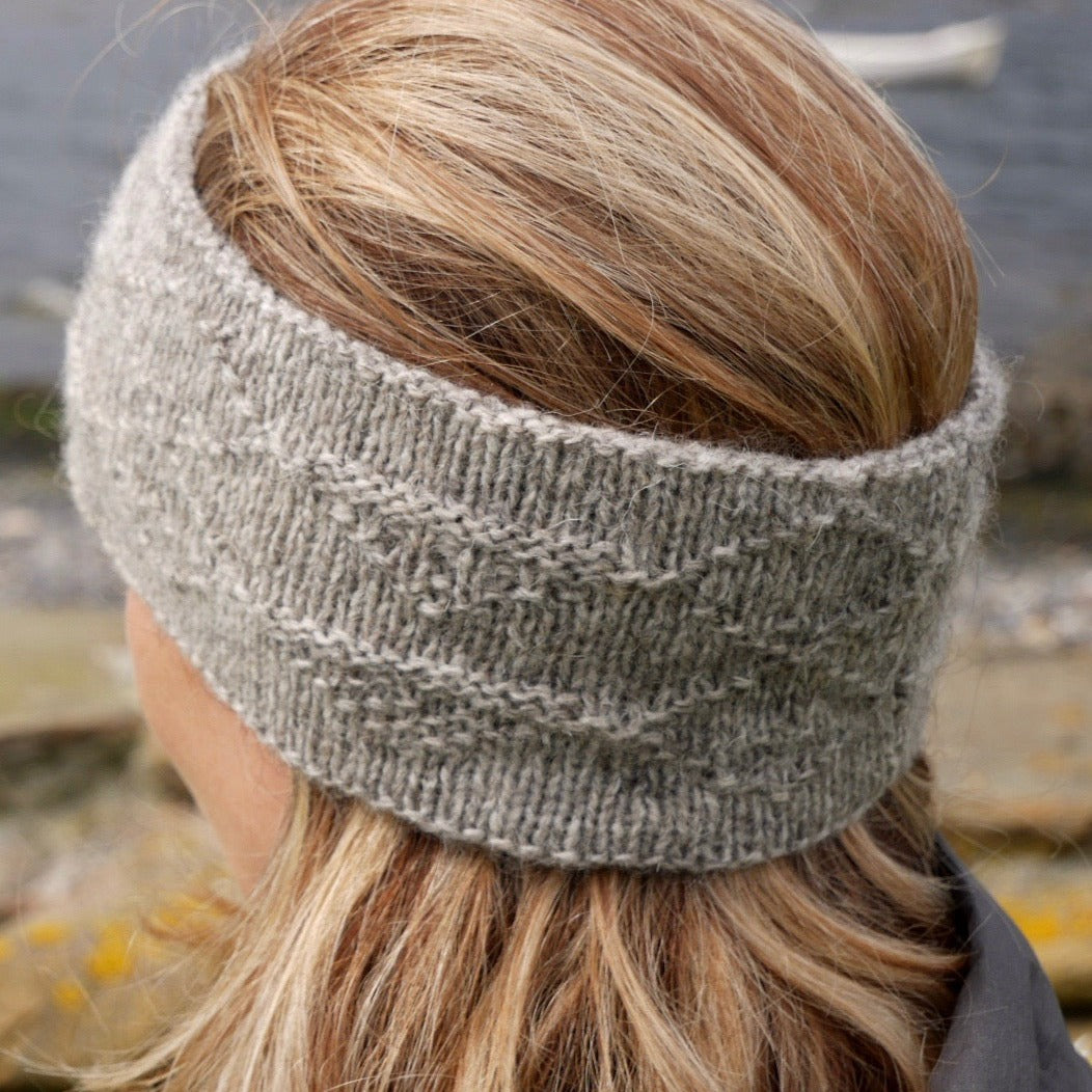 A light gray, knitted headband with a textured pattern.