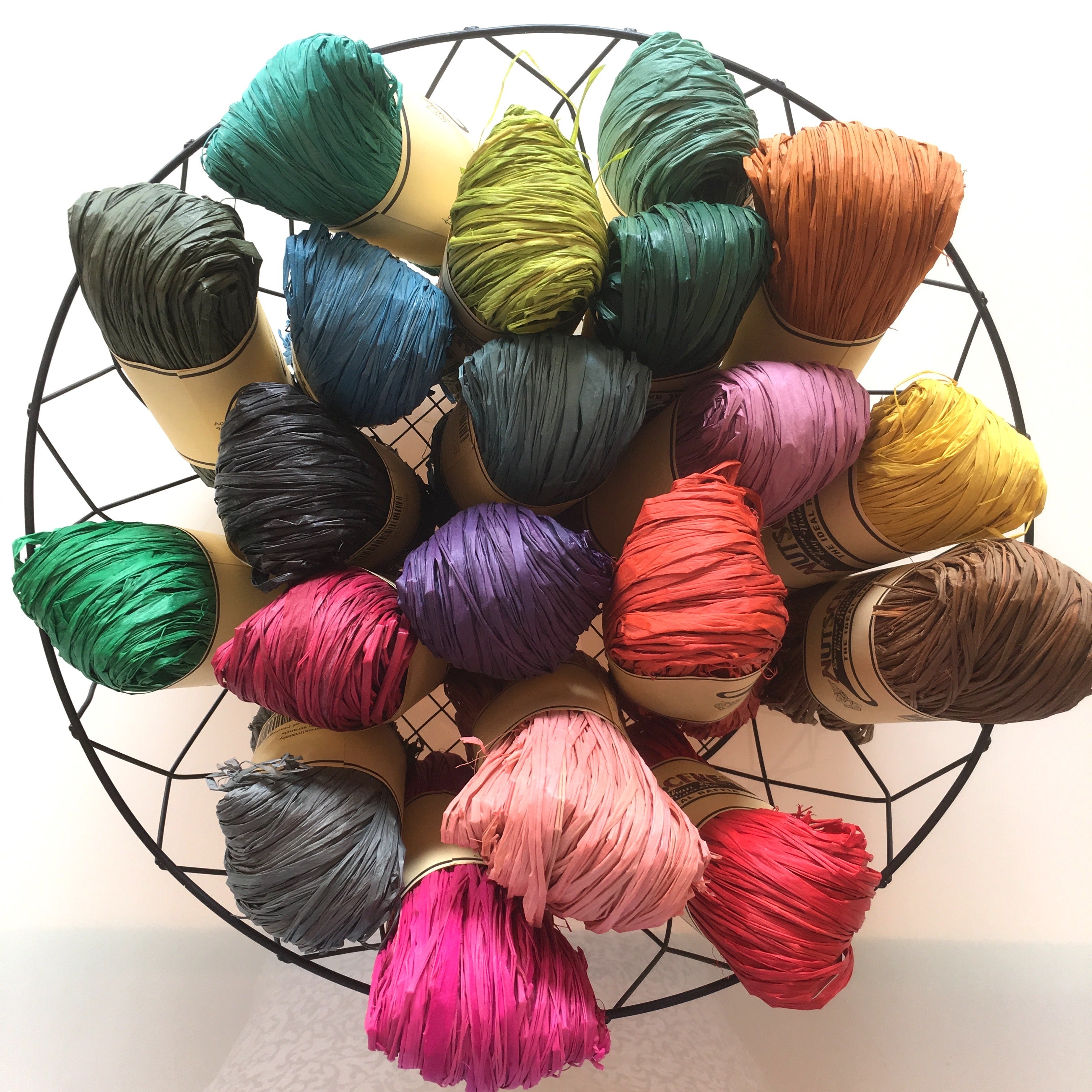 Assortment of colorful shredded paper strands in various shades, displayed on a black wire rack.