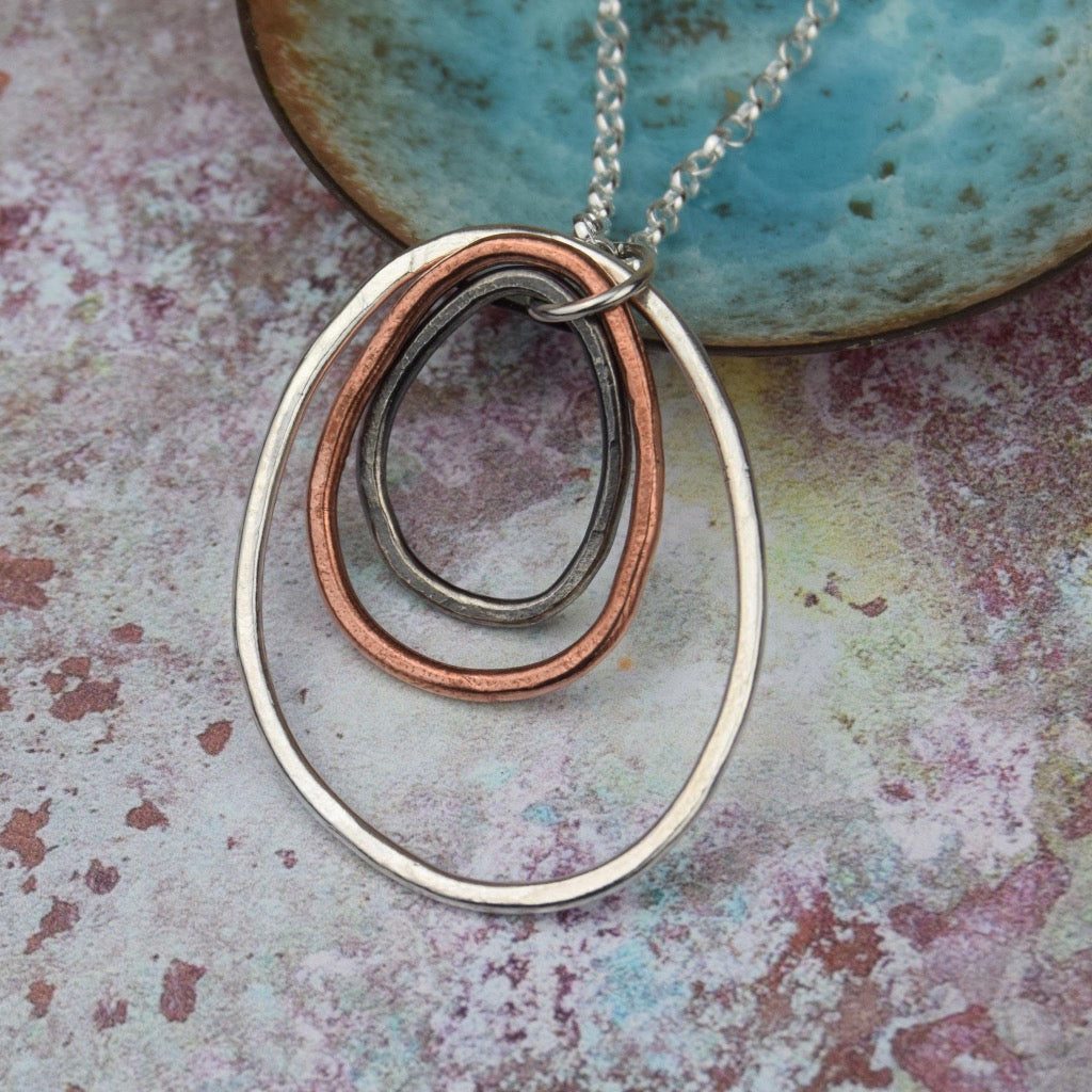Silver necklace with a pendant featuring three interlocking oval shapes in silver, copper, and dark metal.