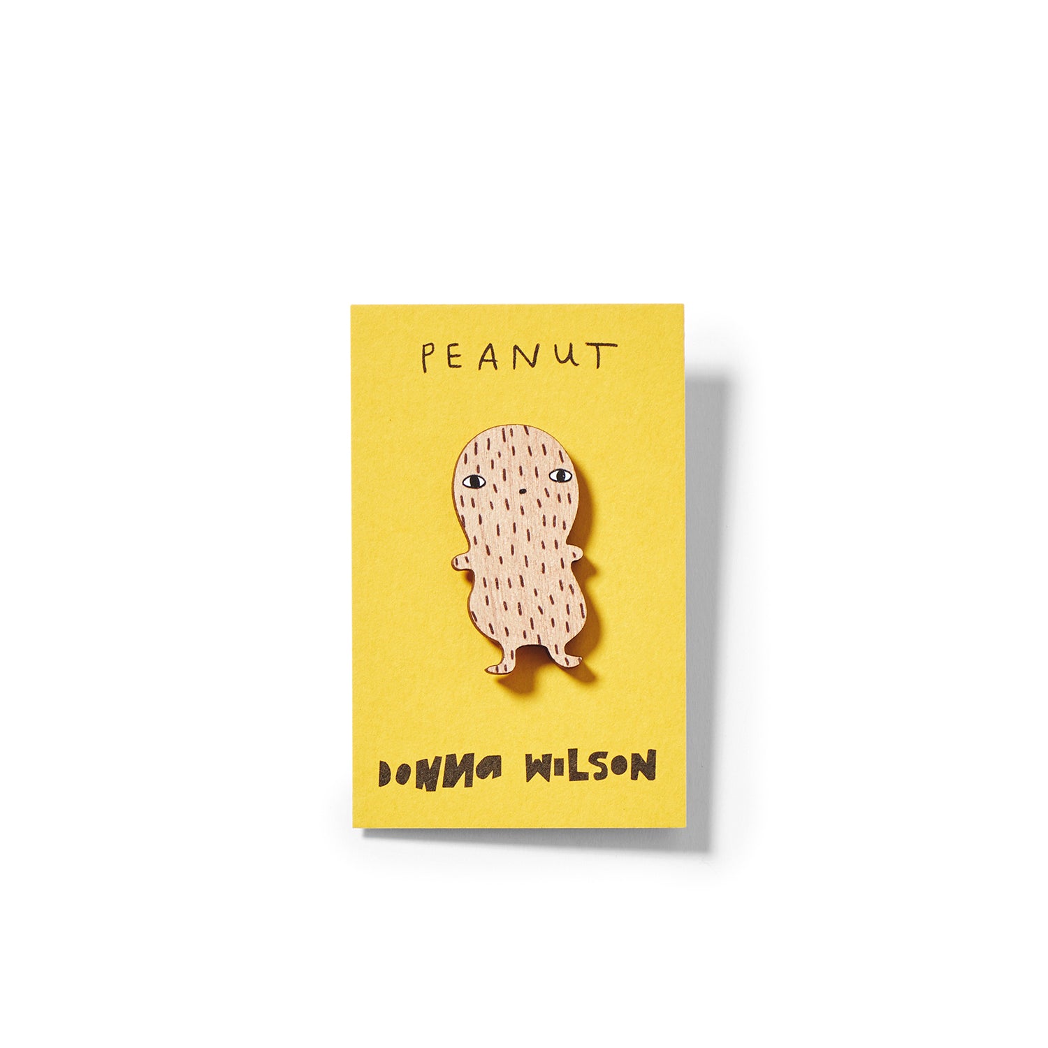 A wooden peanut character in light brown, on a yellow card labeled "Peanut" by Donna Wilson.