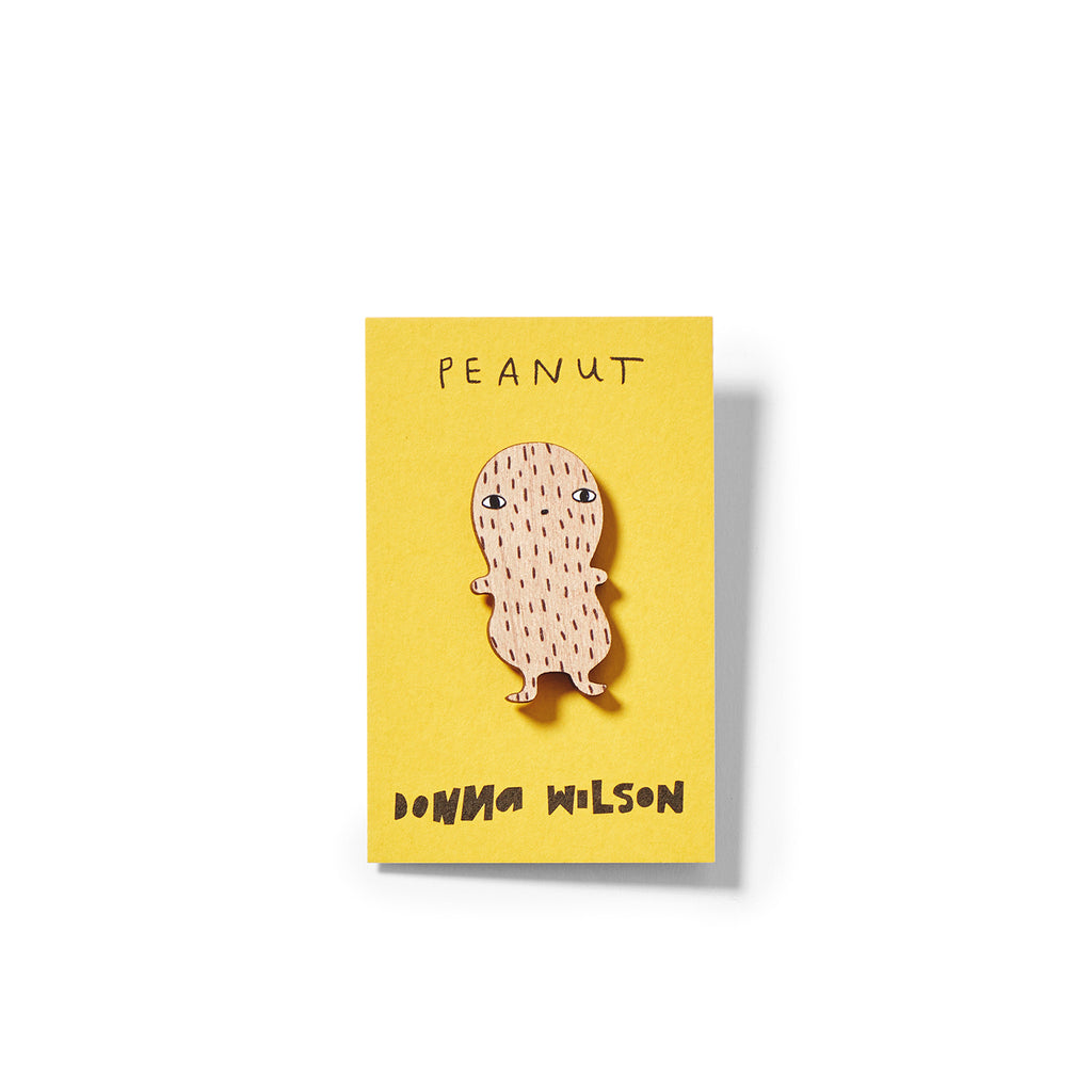 A wooden peanut character in light brown, on a yellow card labeled "Peanut" by Donna Wilson.