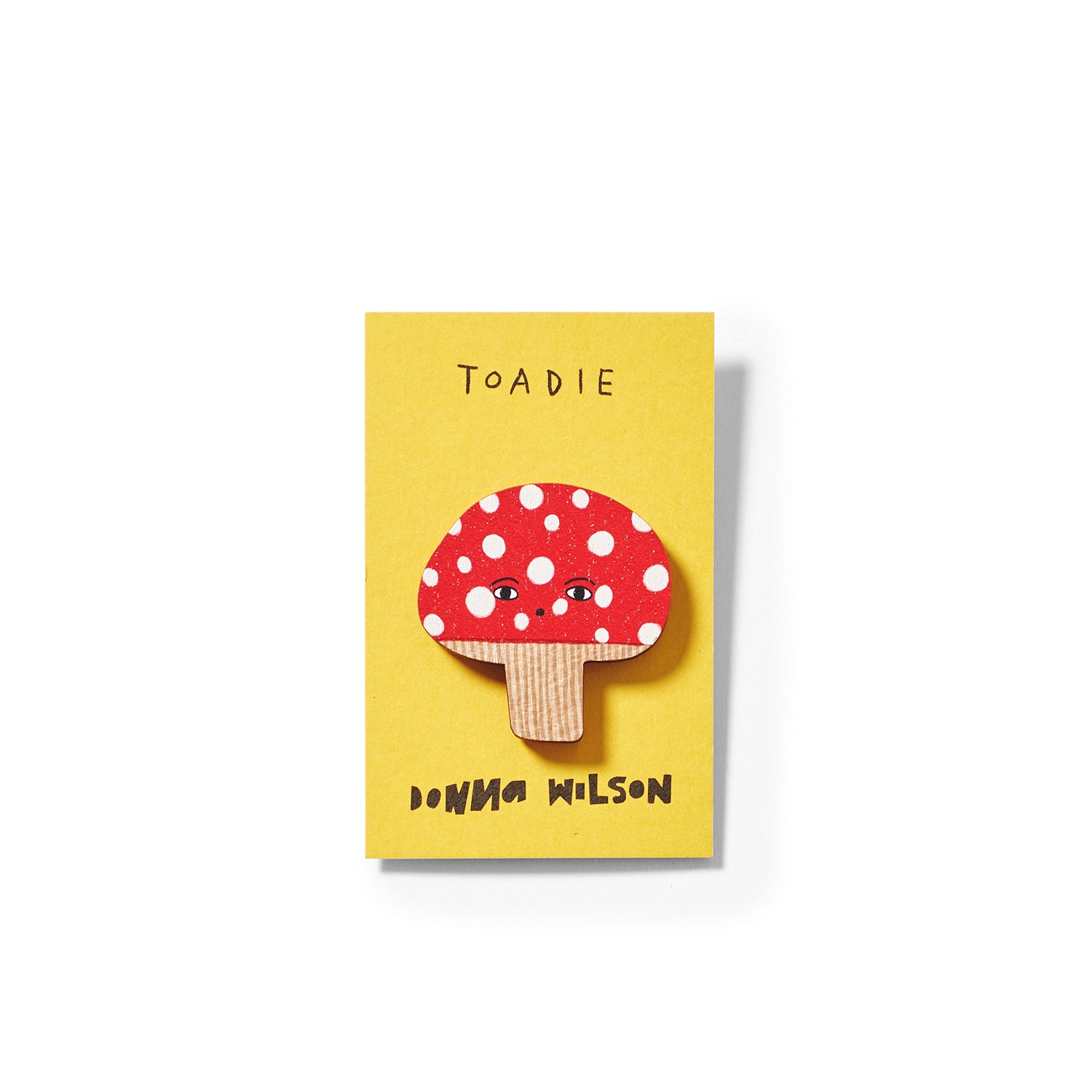 A yellow card featuring a red mushroom with white spots, labeled "Toadie," by Donna Wilson.