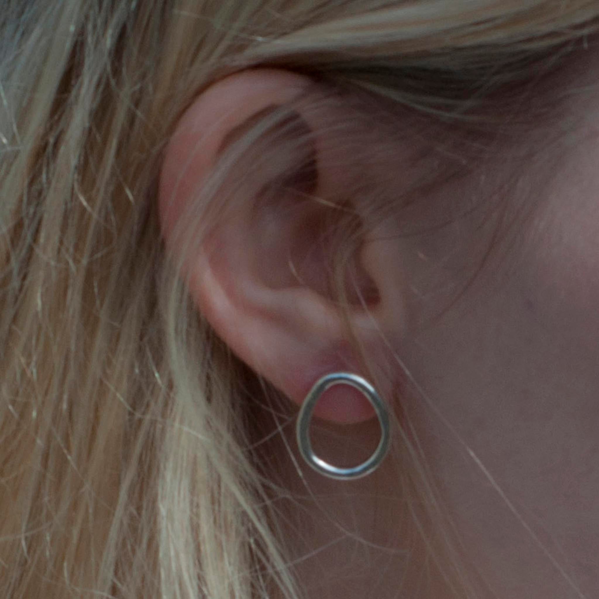 Close-up of a person's ear wearing a simple, silver, oval-shaped stud earring.