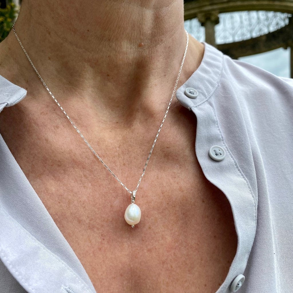 Silver chain necklace with a single, large, off-white pearl pendant.