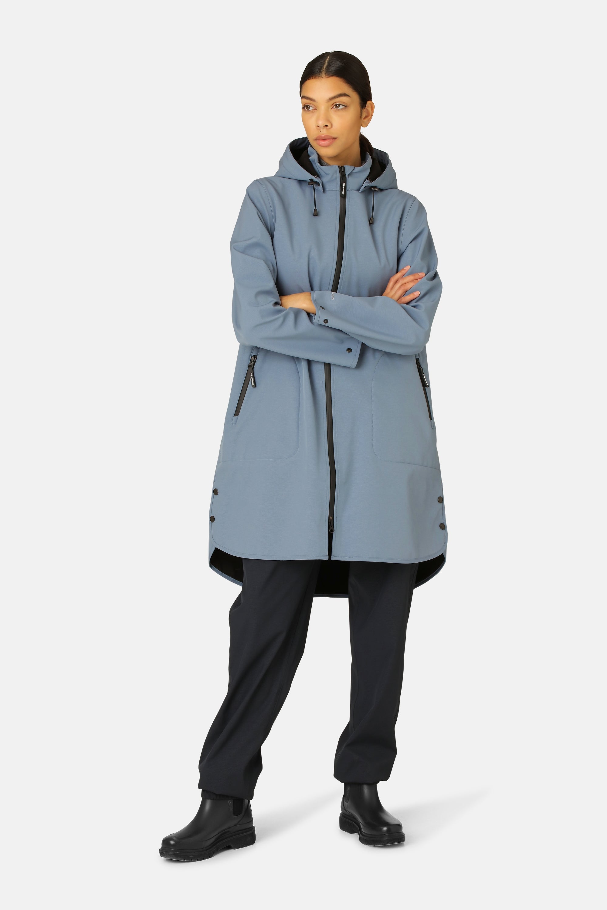 Woman in a long, light blue waterproof Rains jacket with a black zipper and hood, black pants, and black Chelsea boots.