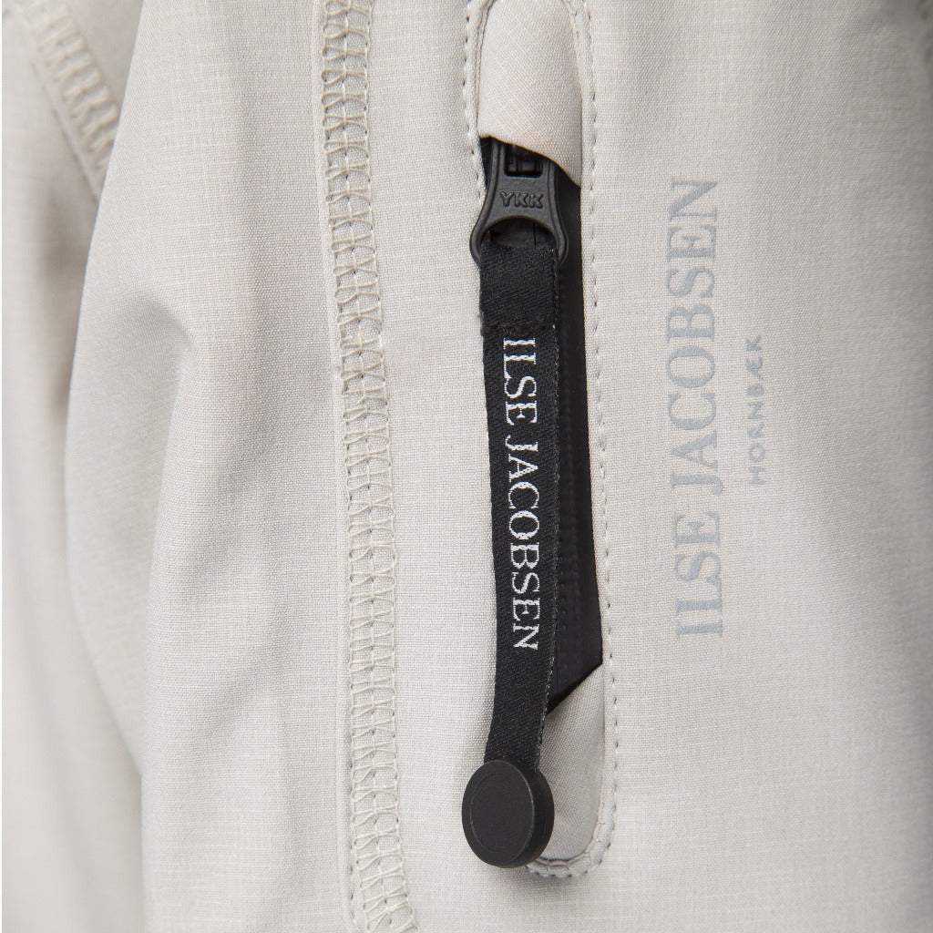 Close-up of Ilse Jacobsen Hornbæk light grey jacket detail: zipper with black pull tab featuring brand logo.