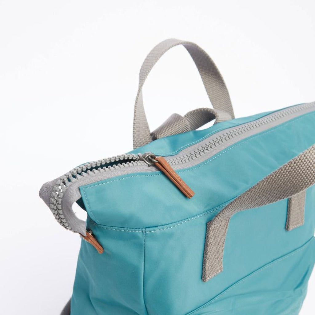 Teal blue backpack with gray straps and a top zipper closure. The zipper pull is light brown.