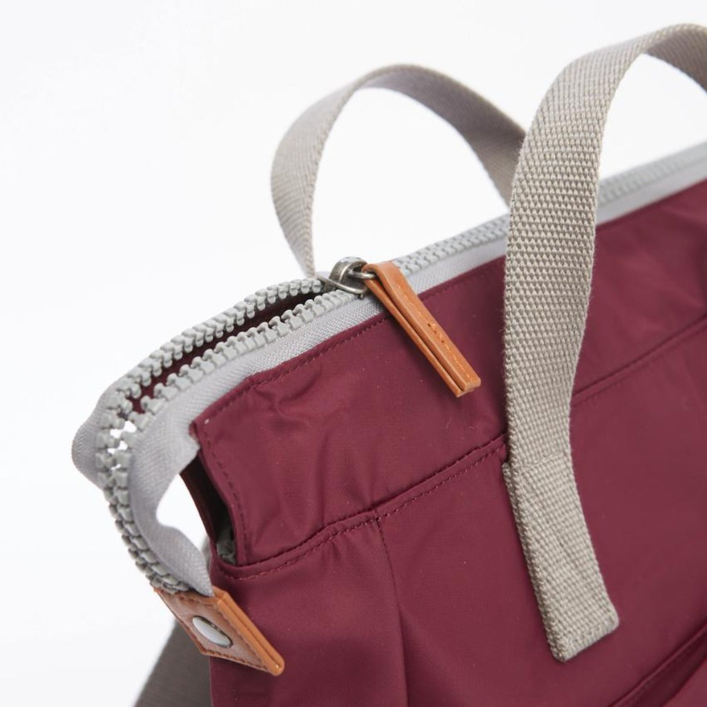 Burgundy handbag with gray straps and a top zipper closure; accented with light brown leather zipper pulls.