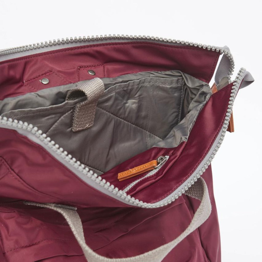 Burgundy tote bag with gray zipper and handles, showing quilted gray interior lining and small leather zipper pull.