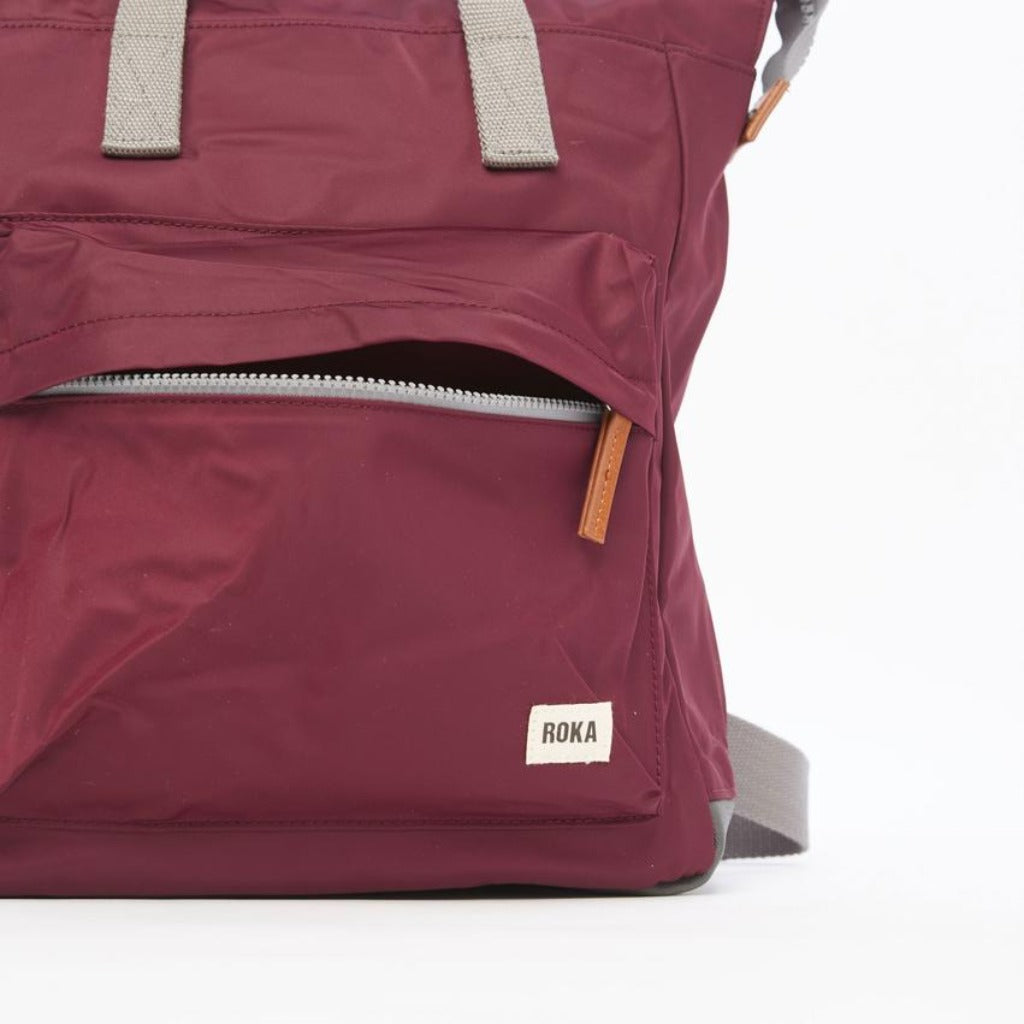 Burgundy RoKa backpack with grey accents and a small front zipper pocket. The brand label is visible.
