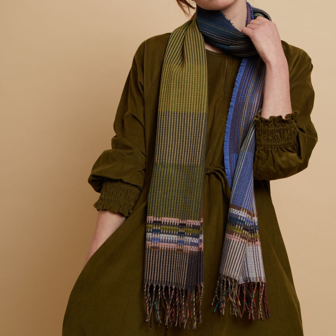 Multicolored striped wool scarf with fringed edges.  The scarf features shades of green, blue, and beige in a woven pattern.