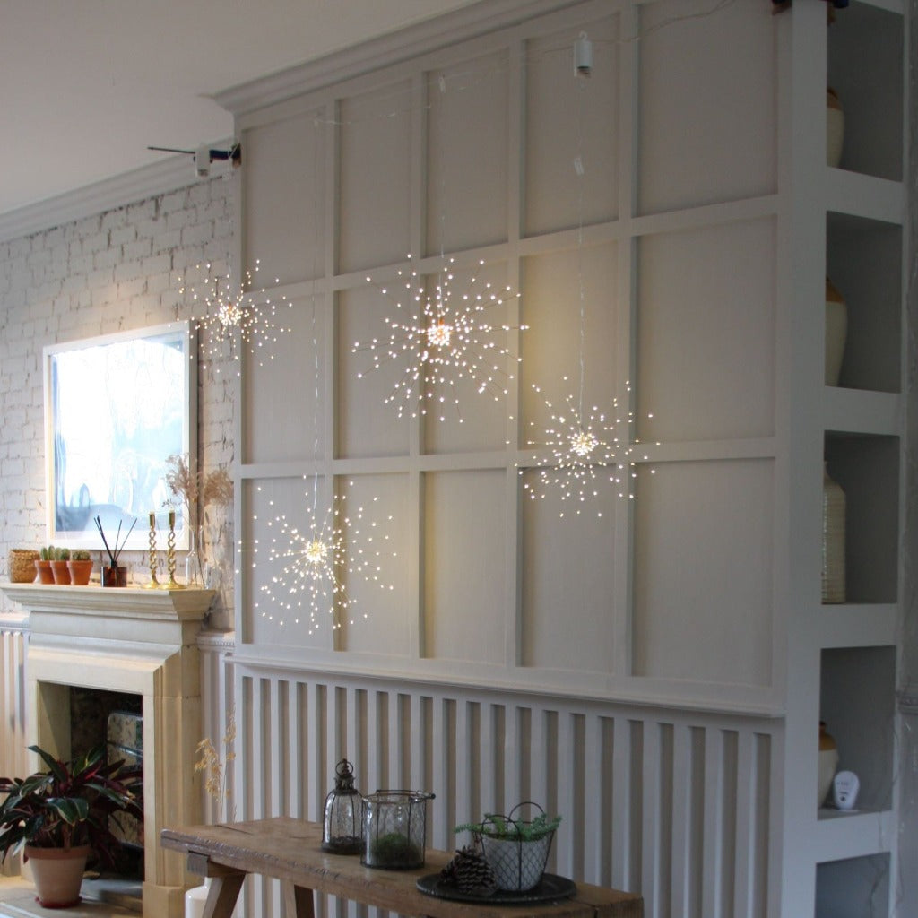 Five firework-shaped LED string lights hanging against a light gray paneled wall.