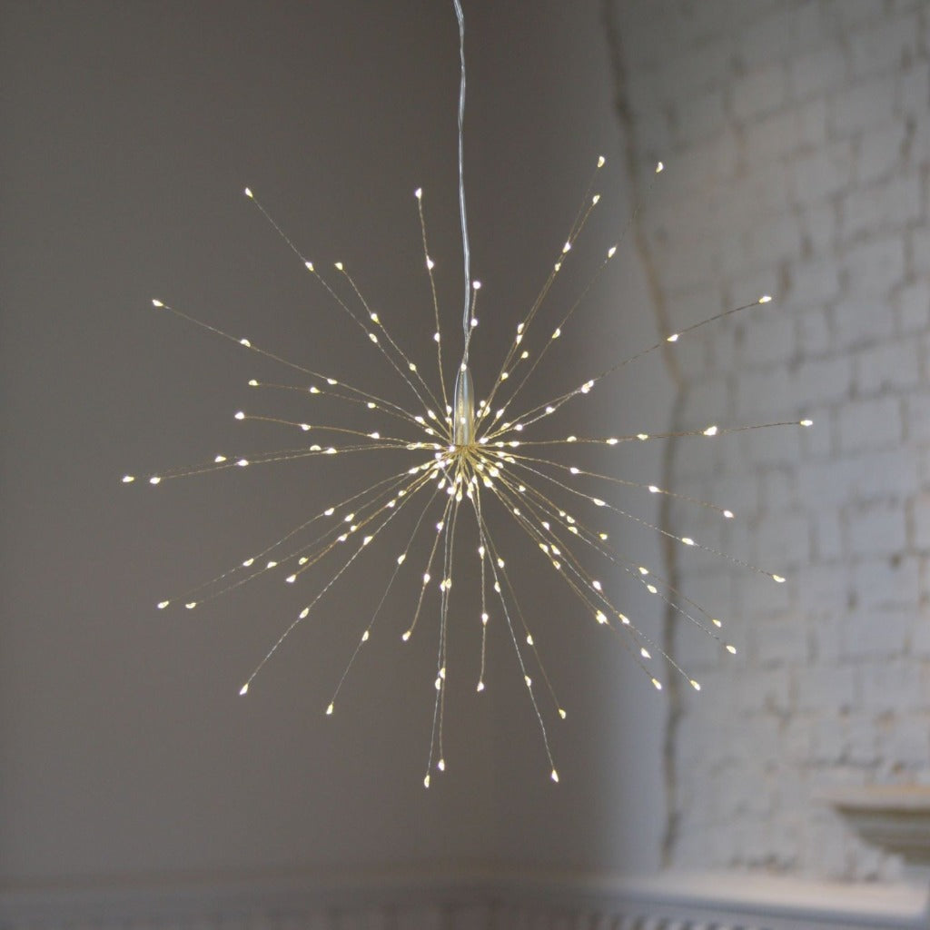 LED firework light fixture with numerous thin wires radiating from a central point, emitting warm white light.